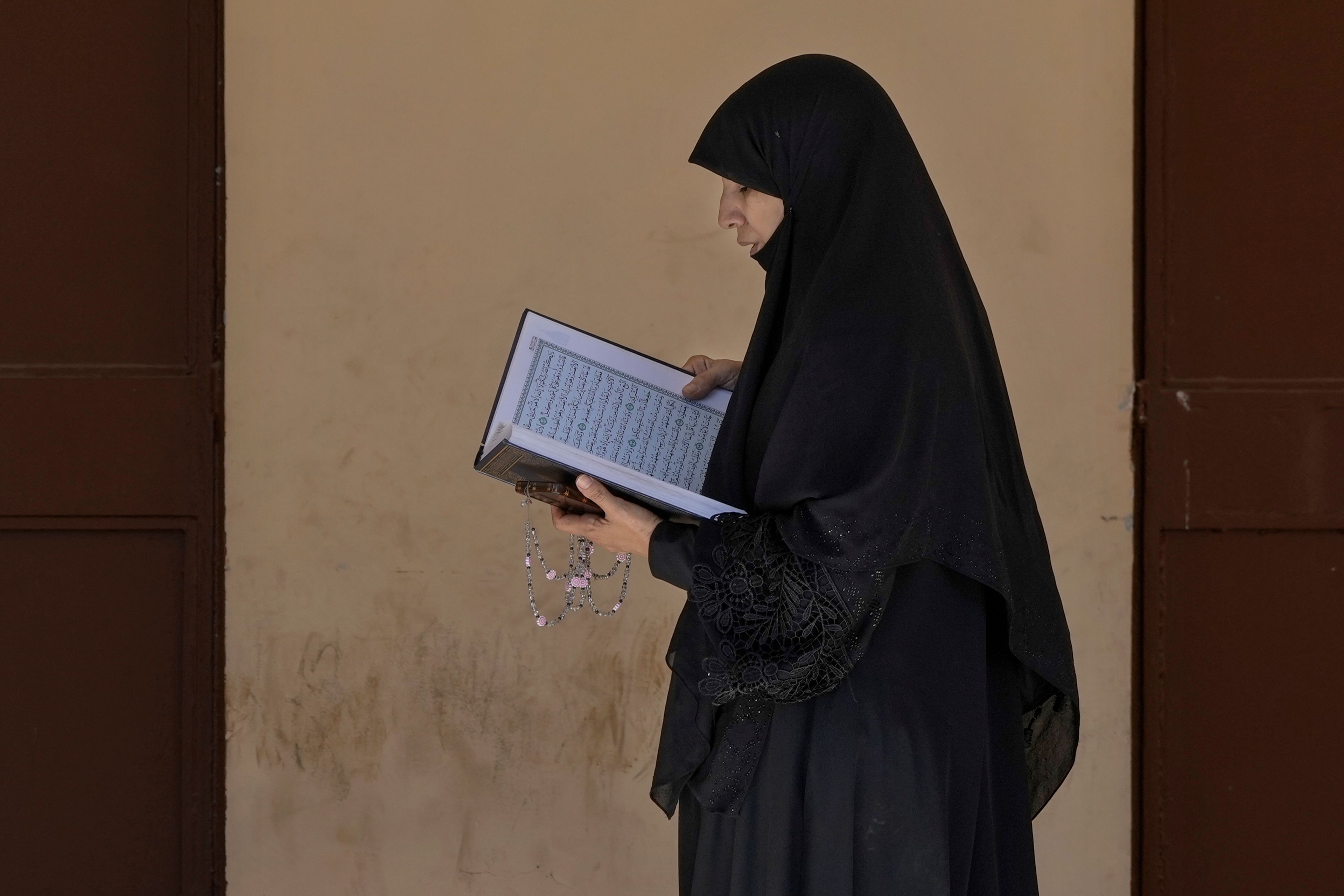 A displaced woman reads a Quran, the Muslim holy book, at a vocational training center run by the U.N. agency for Palestinian refugees, or UNRWA, in the town of Sebline, south of Beirut, Lebanon, Friday, Oct. 4, 2024, after fleeing the Israeli airstrikes in the south. (AP Photo/Bilal Hussein)