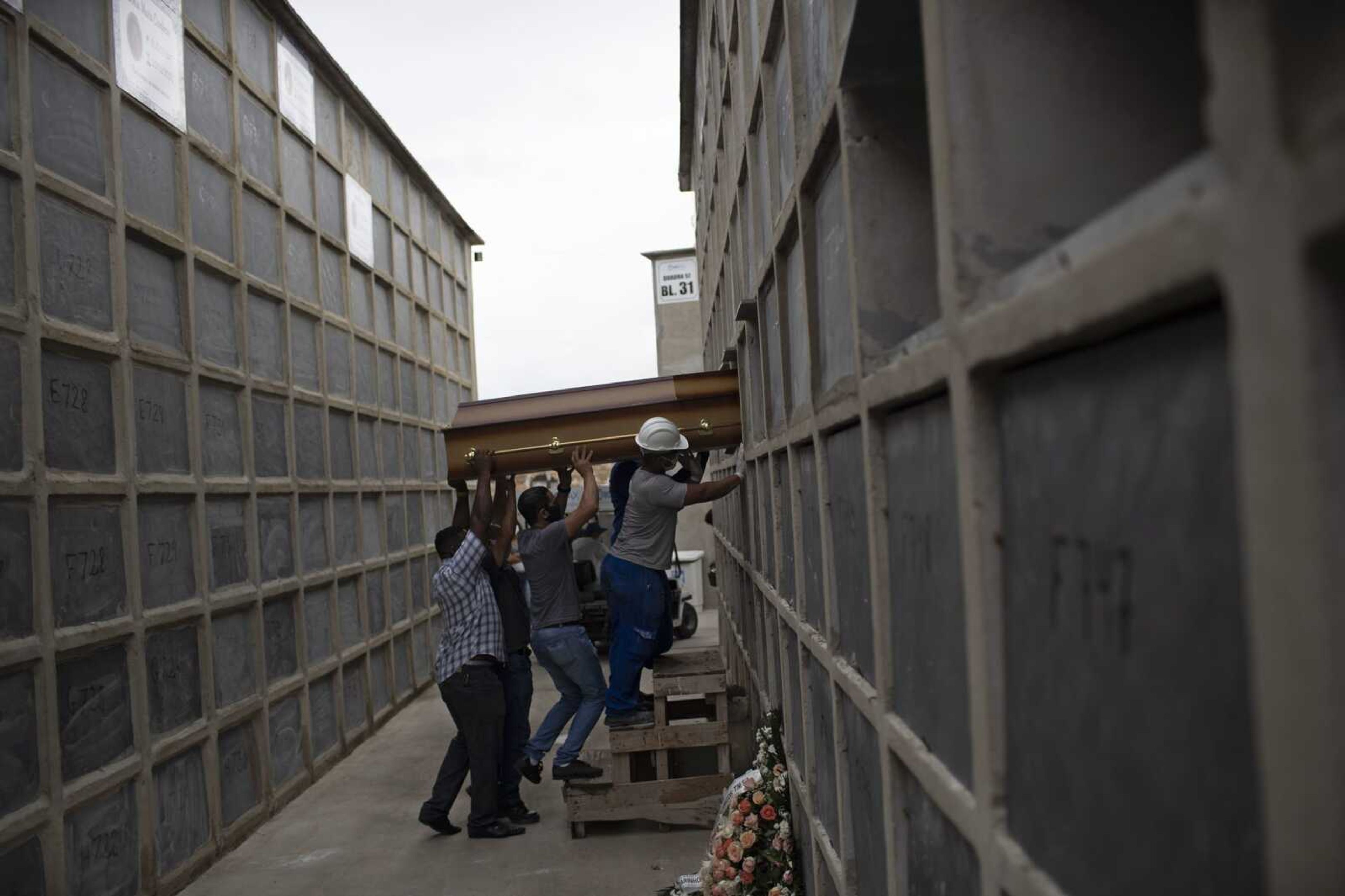 The coffin containing the remains a woman who died from complications related to COVID-19 is placed into a niche by cemetery workers and relatives at the Inahuma cemetery Tuesday in Rio de Janeiro, Brazil.