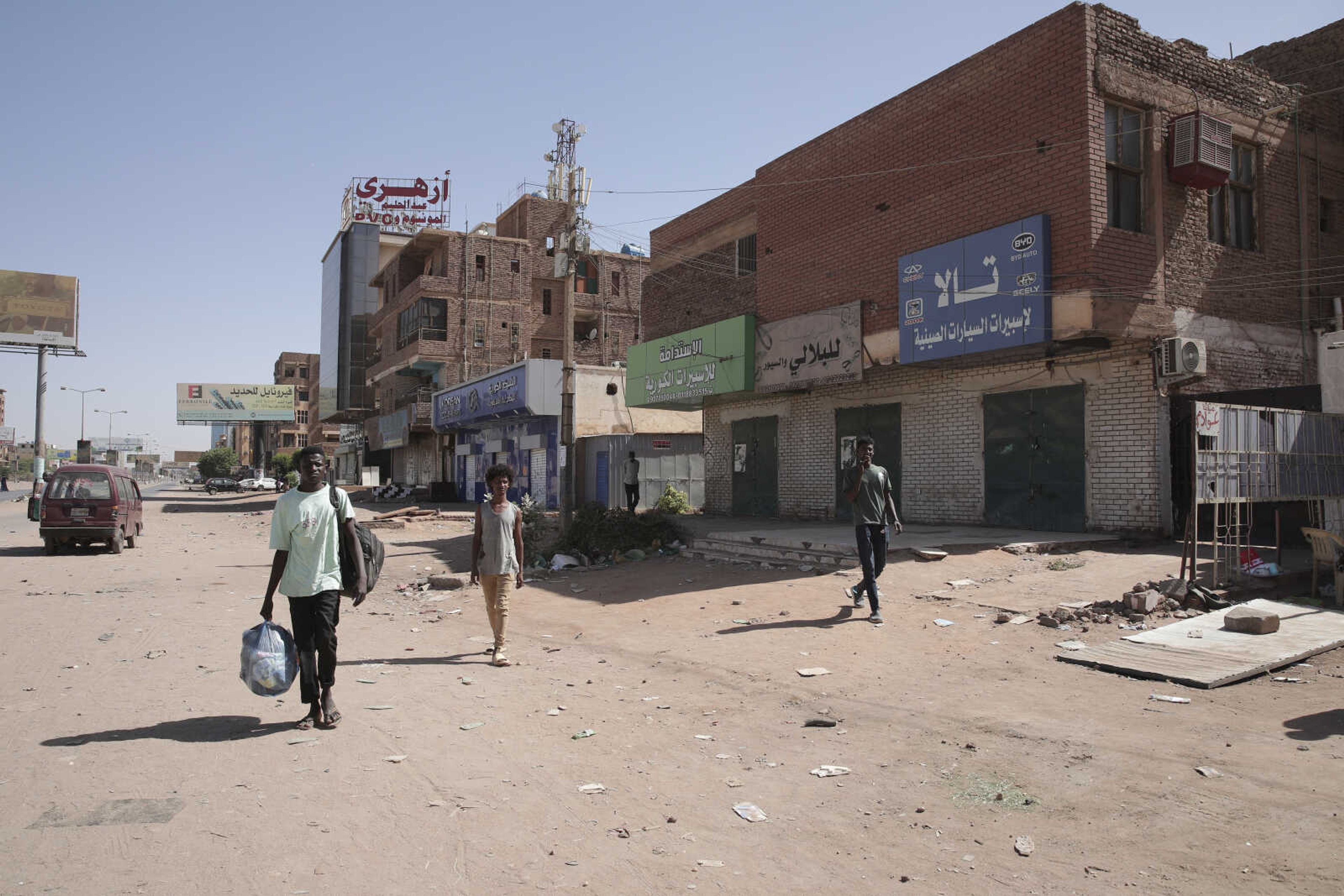 People walk past shuttered shops Tuesday in Khartoum, Sudan. Sudan's embattled capital awoke to a fourth day of heavy fighting between the army and a powerful rival force for control of the country. Airstrikes and shelling intensified Monday in parts of Khartoum and the adjoining city of Omdurman.