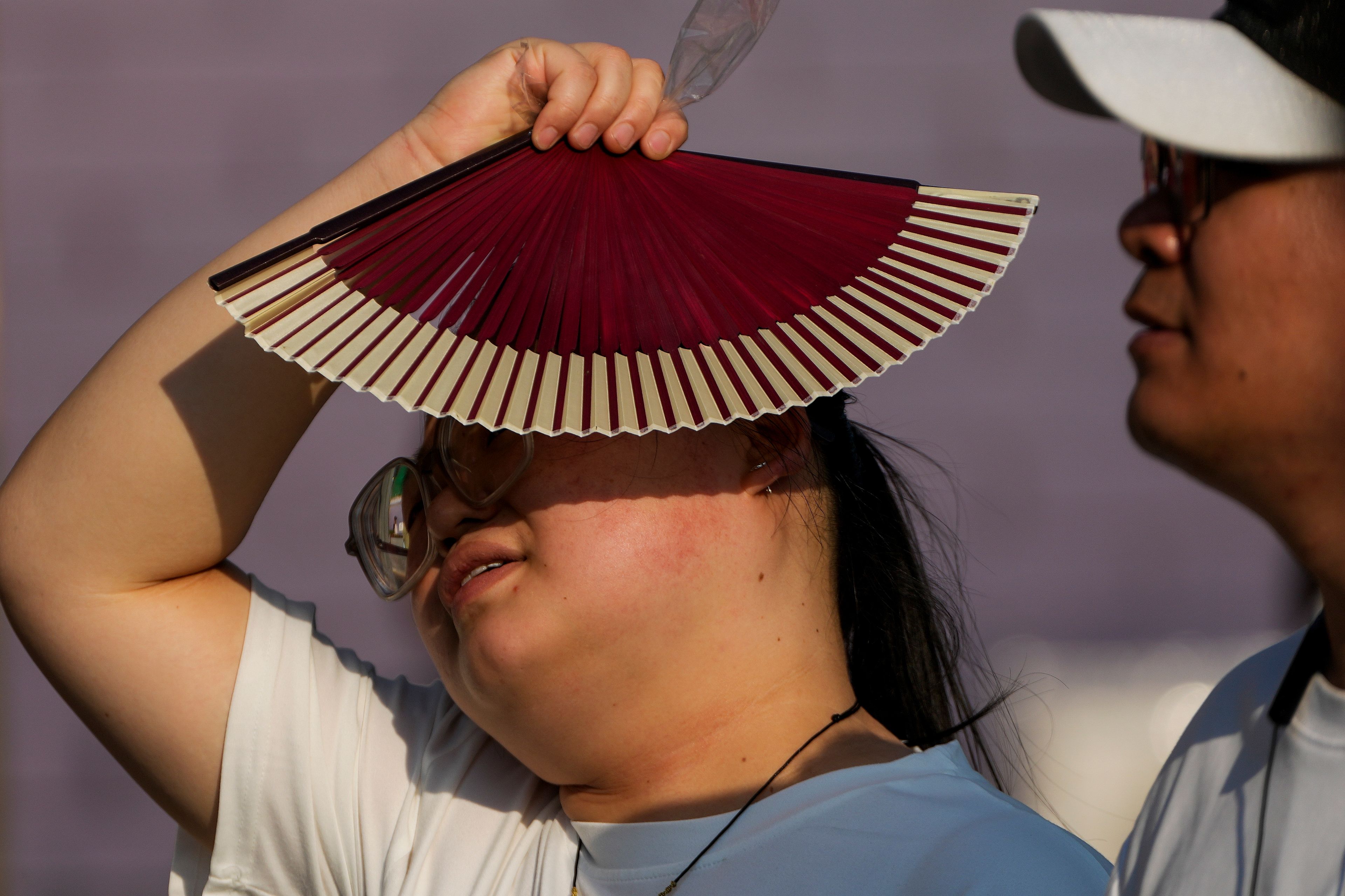 FILE - A woman uses a fan to block the sun as she walks with her companion on a hot day in Beijing, June 16, 2024. (AP Photo/Andy Wong, File)