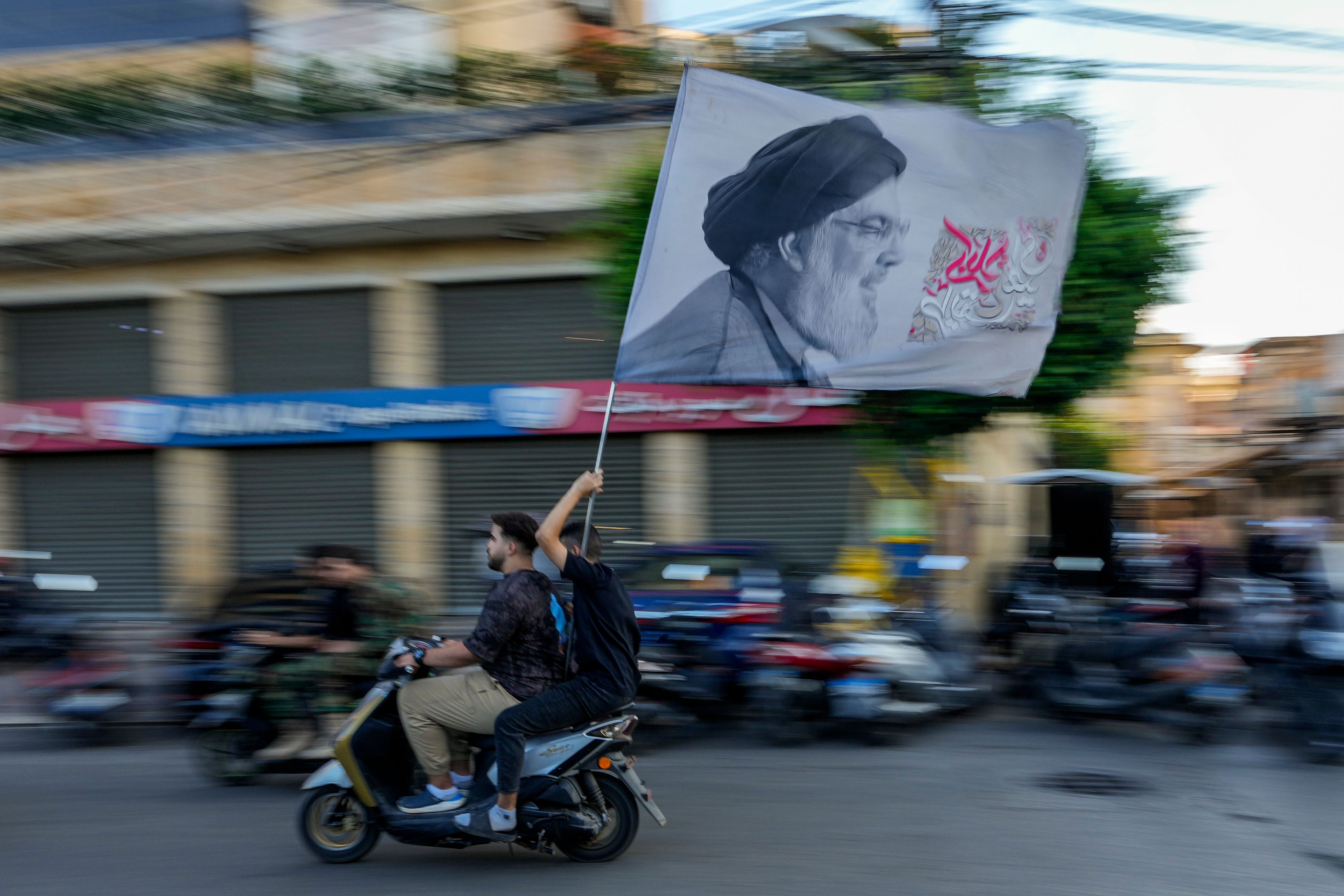 Hezbollah supporters carry a flag depicting Hezbollah leader Hassan Nasrallah as they ride a scooter following the funeral procession of Hezbollah commanders Ibrahim Kobeisi and Hussein Ezzedine in Beirut's southern suburb, Wednesday, Sept. 25, 2024. (AP Photo/Hassan Ammar)