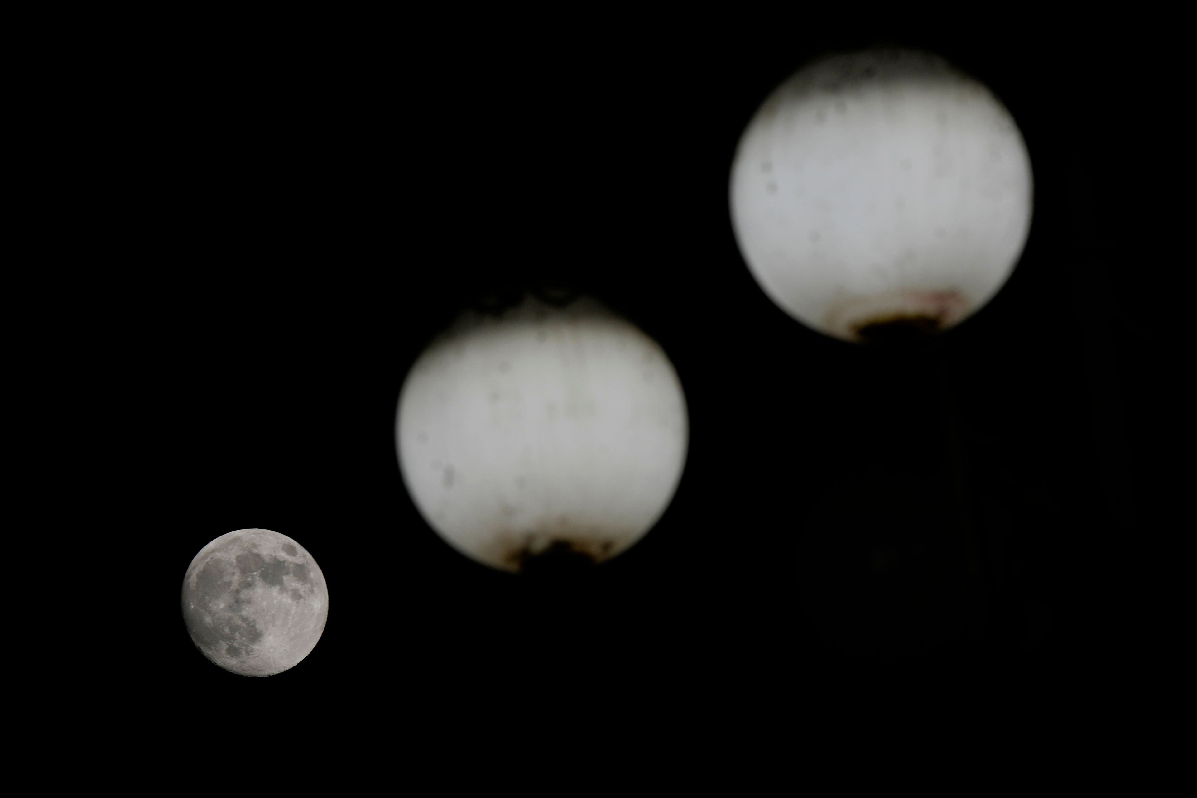 The moon rises behind street lamps in Milan, Italy, Thursday, Nov. 14, 2024. (AP Photo/Luca Bruno)