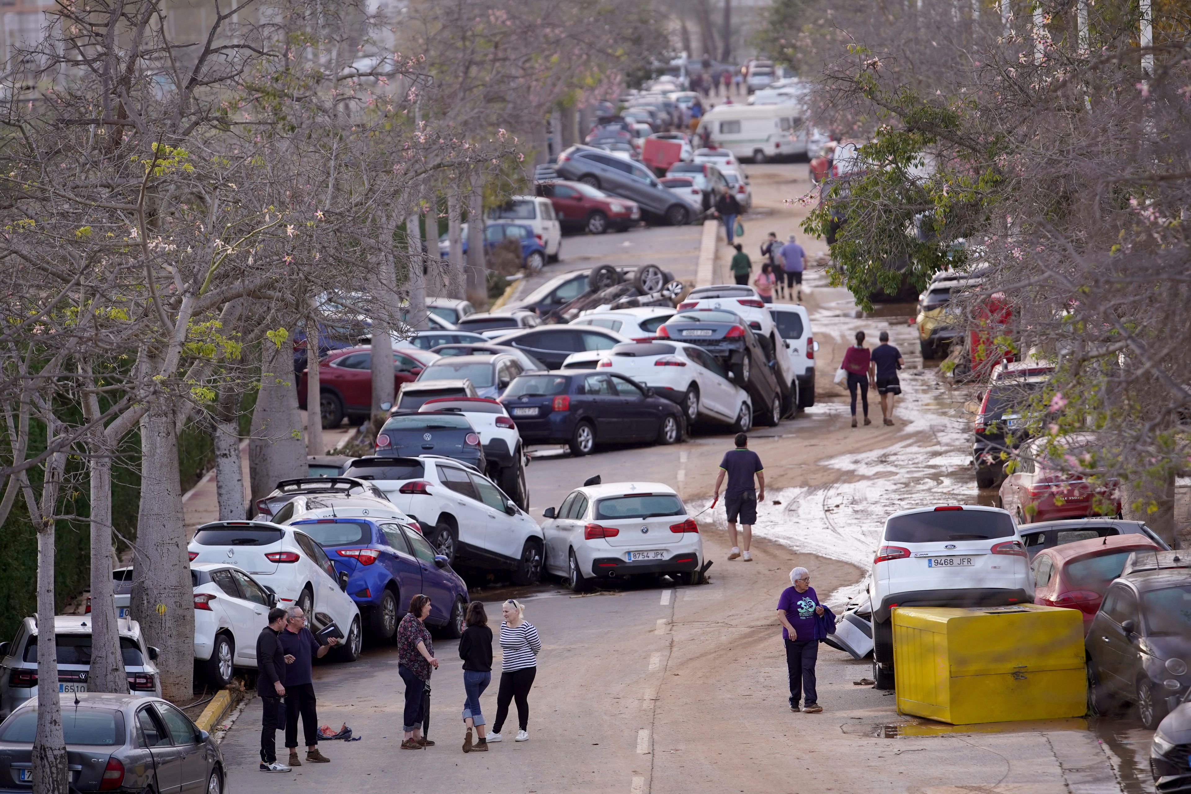 Residents walk next to cars piled up after being swept away by floods in Paiporta, near Valencia, Spain, Wednesday, Oct. 30, 2024. (AP Photo/Alberto Saiz)