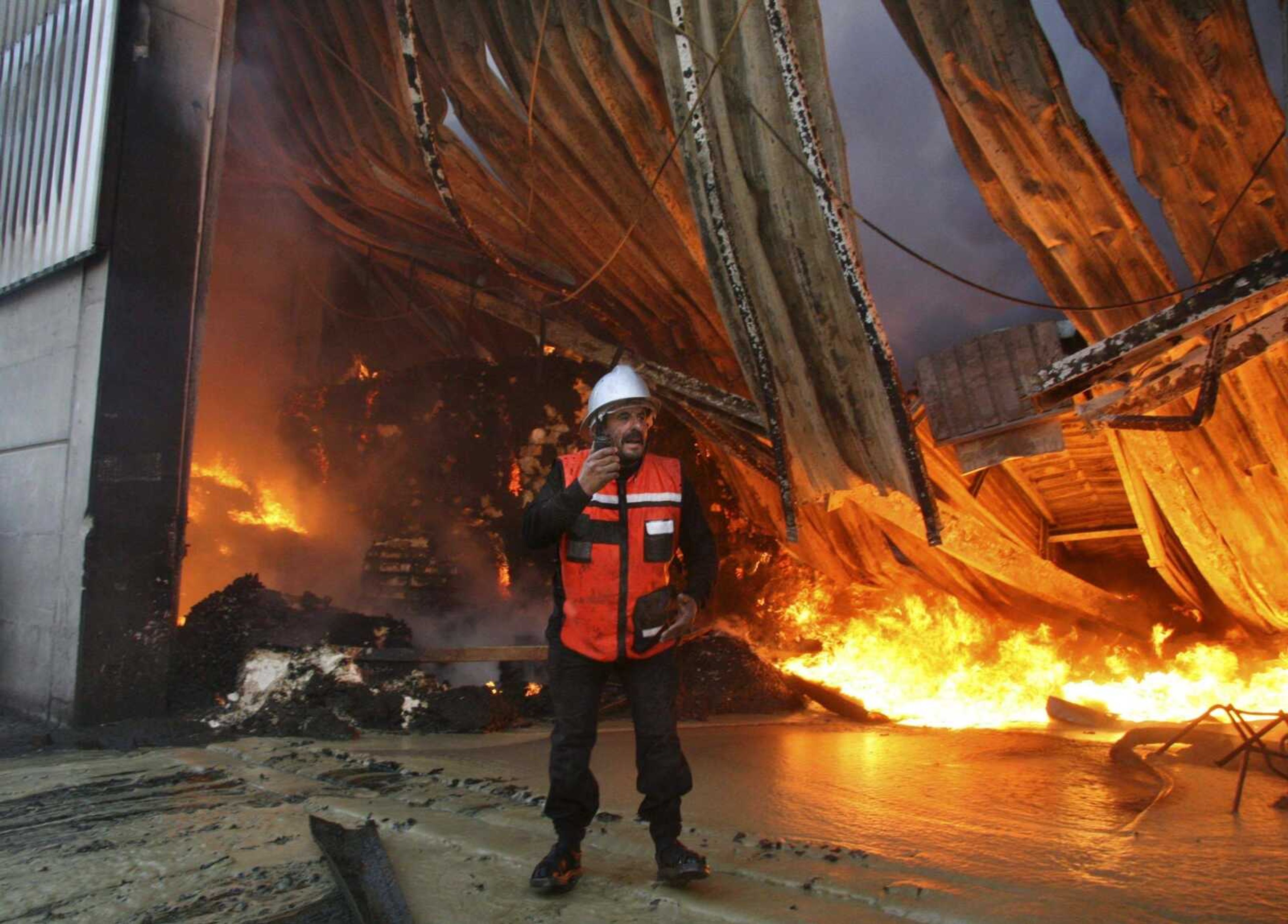 Ashraf Amra ~ Associated Press<br>A Palestinian firefighter talks on a radio Thursday as he and others try to put out a fire at the United Nations headquarters after it was hit in Israeli bombardment in Gaza City.