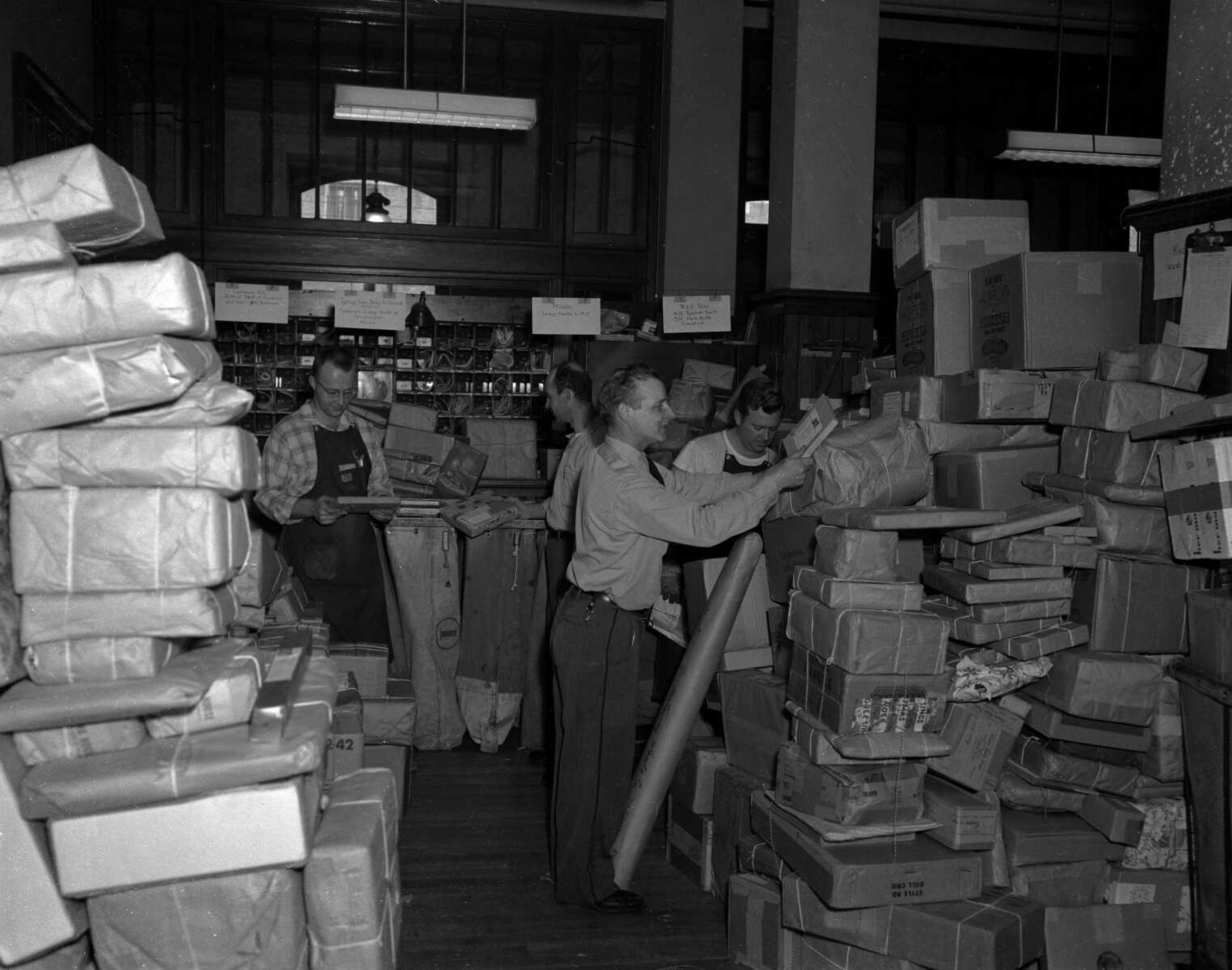 Monday, Dec. 23, 1957, pg. 1
Last roundup. Postoffice employees were deluged today with the final big avalanche of Christmas packages and late mailers sent their gifts on the way. From the left, Clerks Robert J. Sander, Robert D. Gladish, Lee Moore and Weldon Hoeller tackle the mountain of packages.