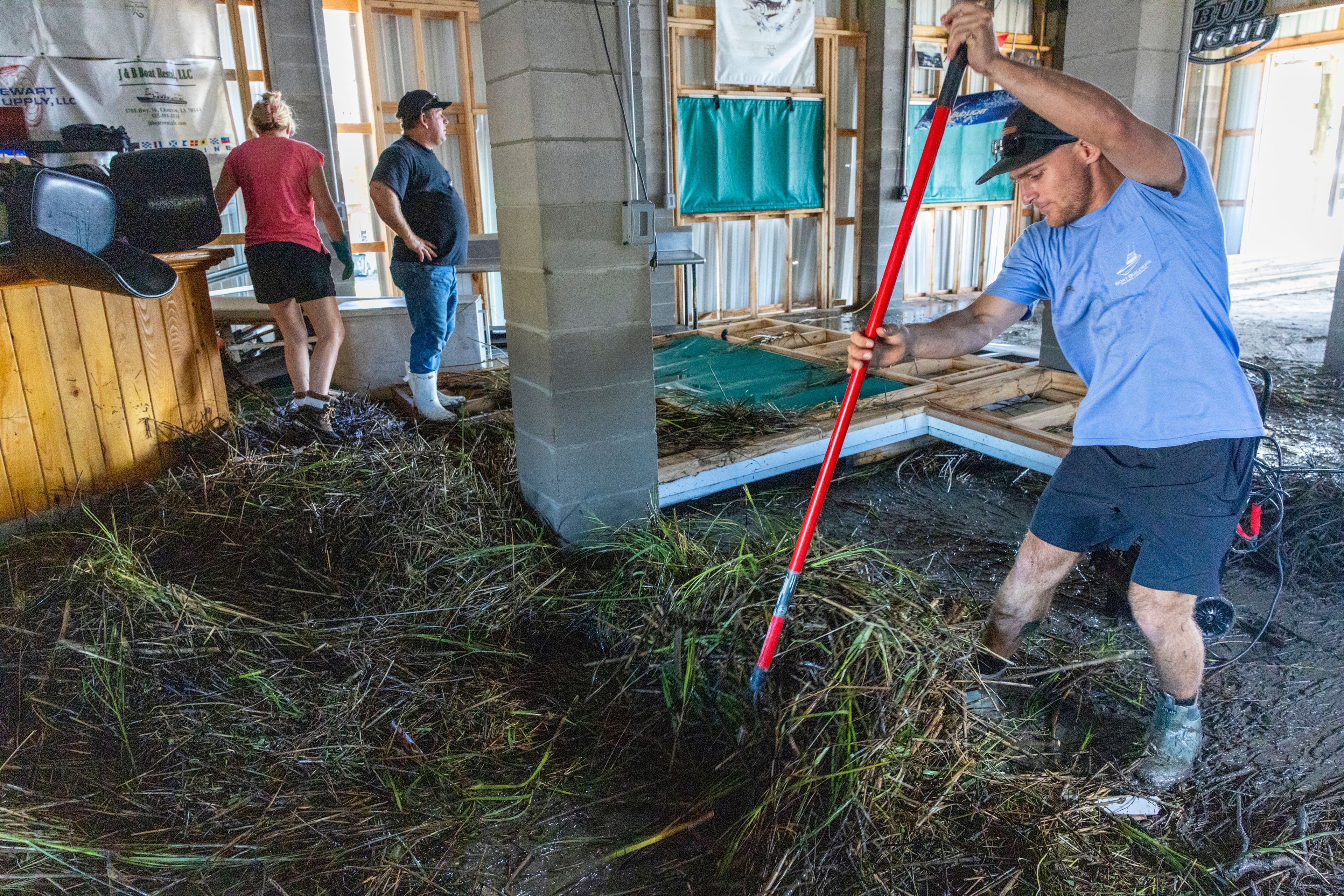 Jansen Pellegrin, right, rakes away marsh grass that floated into a living room area at his family's fishing camp from Hurricane Francine in Terrebonne Parish, La., Thursday, Sept. 12, 2024. (Chris Granger/The Times-Picayune/The New Orleans Advocate via AP)