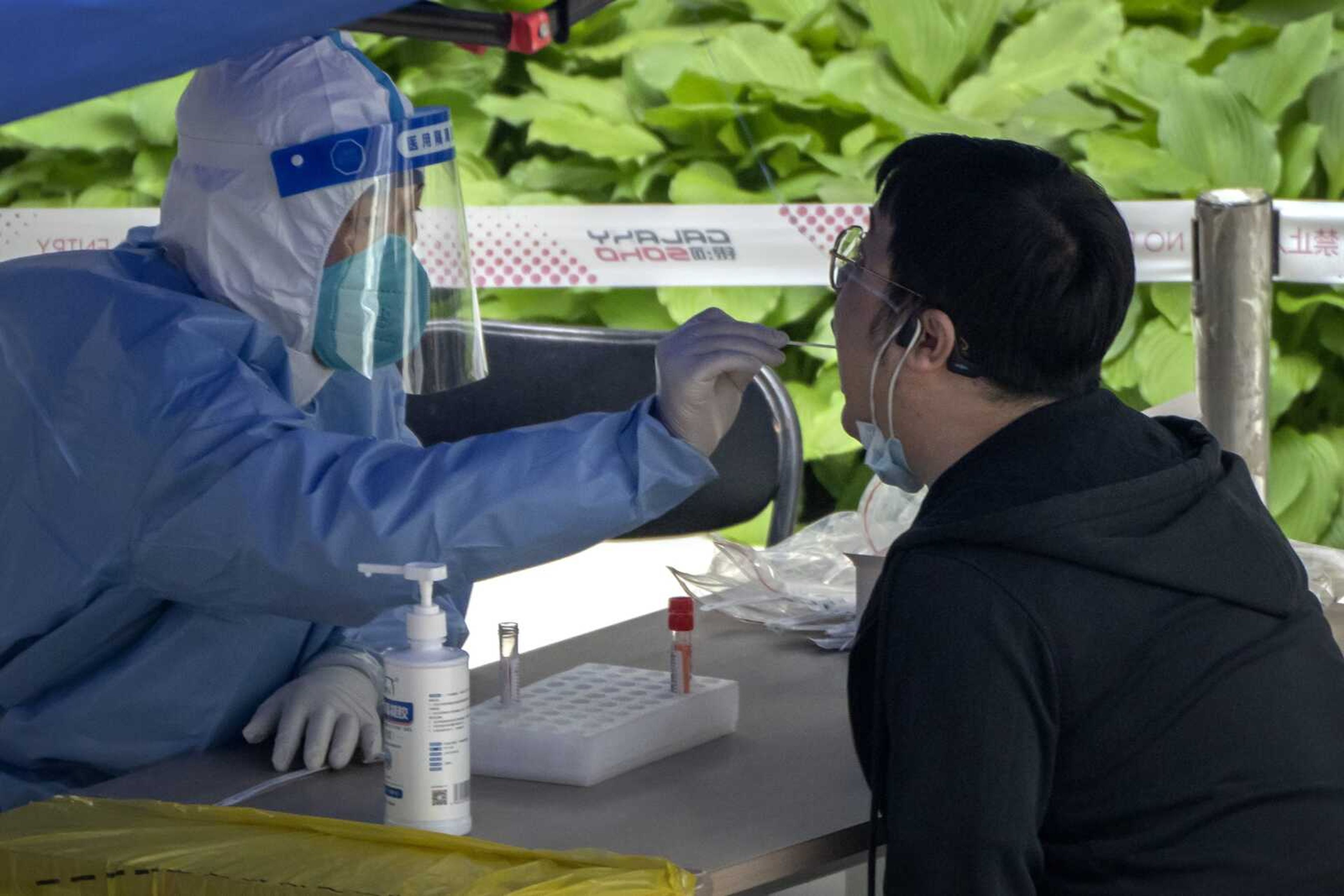 A worker wearing a protective suit swabs a man's throat for a COVID-19 test at a testing site in an office complex in Beijing on Friday.