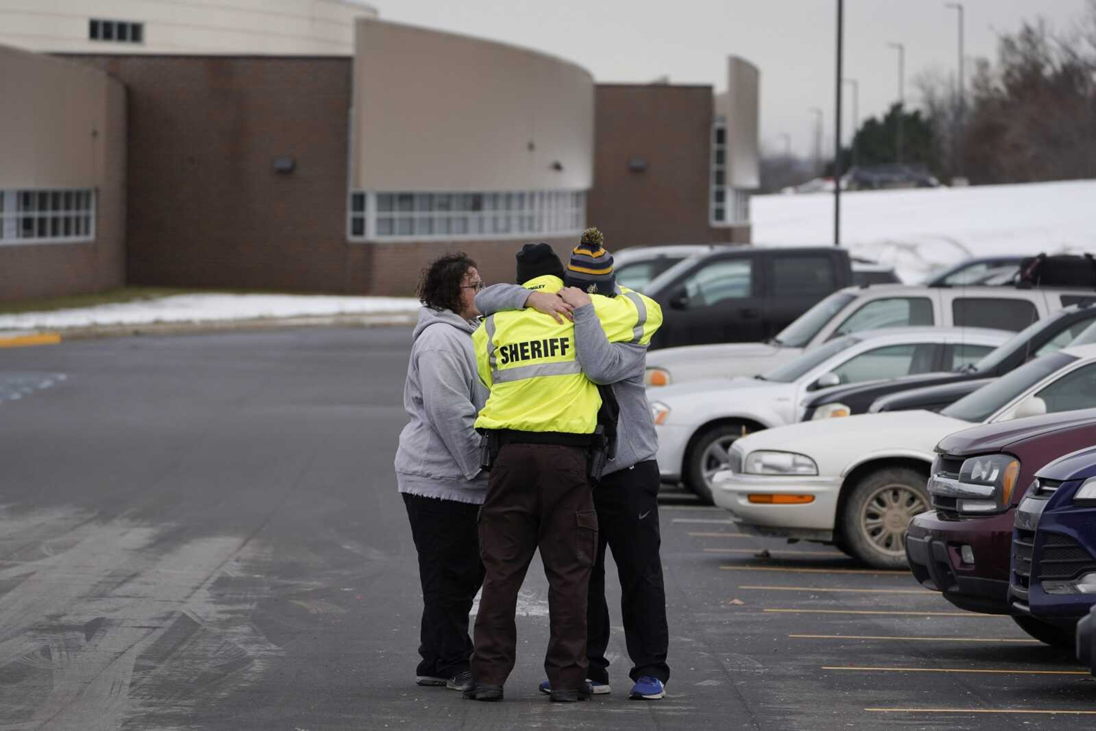 An Oakland County Sheriff's deputy hugs family members of a student in the parking lot of Oxford High School on Wednesday in Oxford, Michigan.