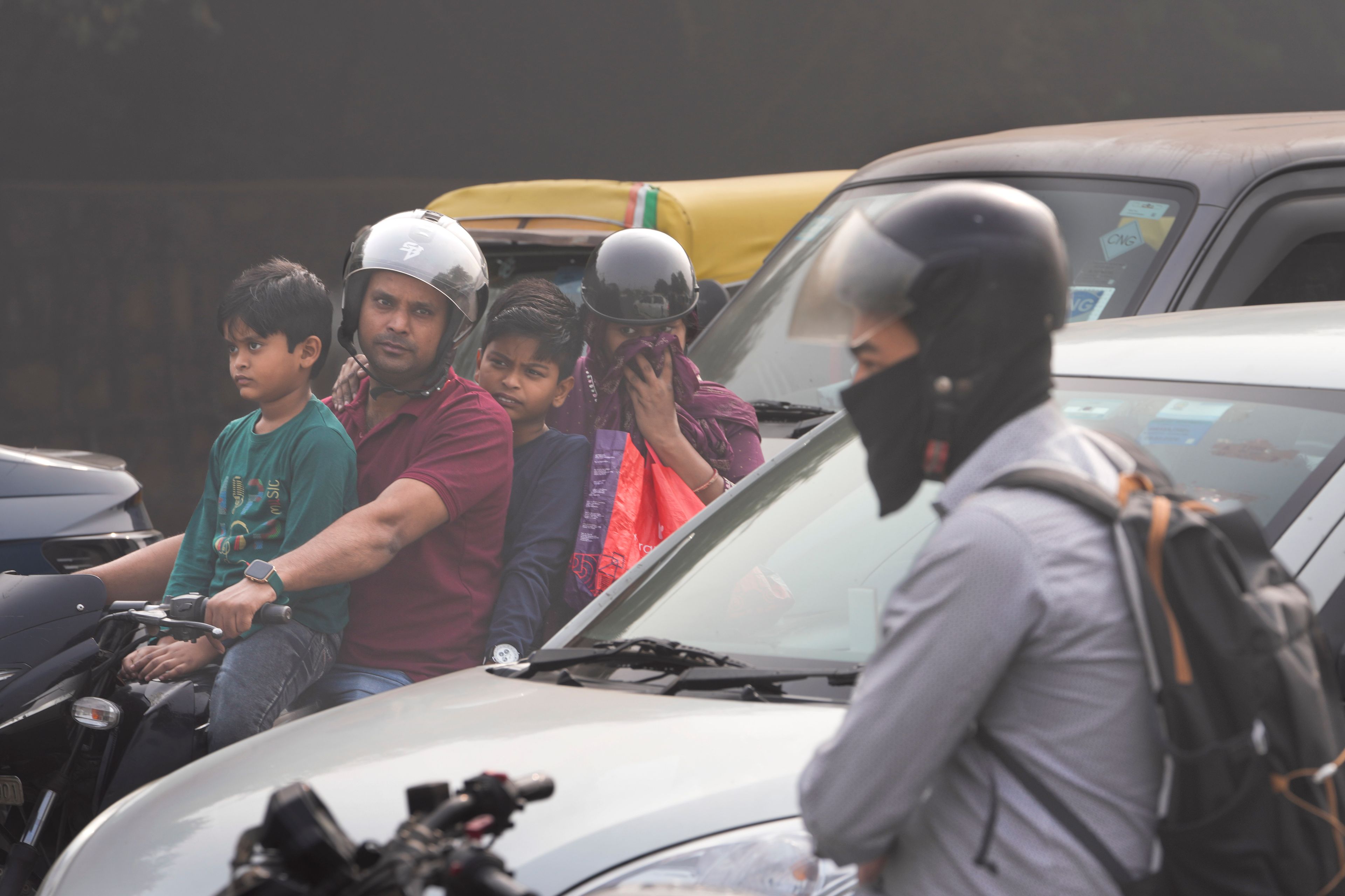 A family on a motorcycle waits at a traffic signal surrounded by smog in New Delhi, India, Thursday, Nov. 14, 2024. (AP Photo/Manish Swarup)