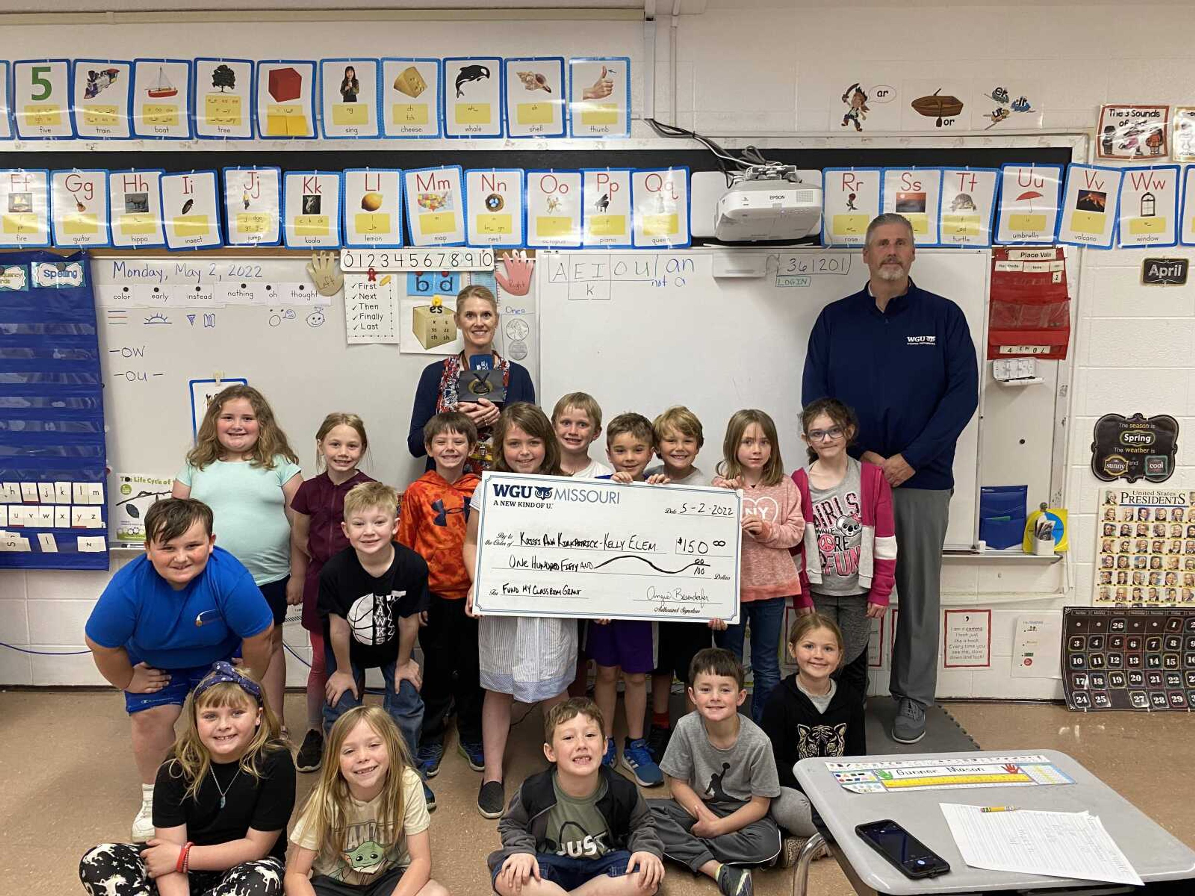 Kristi Ann Kirkpatrick, a first grade teacher at Kelly Elementary School in the Scott County R-IV School District in Benton, poses with her class after learning she had been selected for a $150 grant by WGU Missouri. Jim Chandler, Strategic Partnerships Manager at WGU, surprised Kirkpatrick with the grant in early May. 
