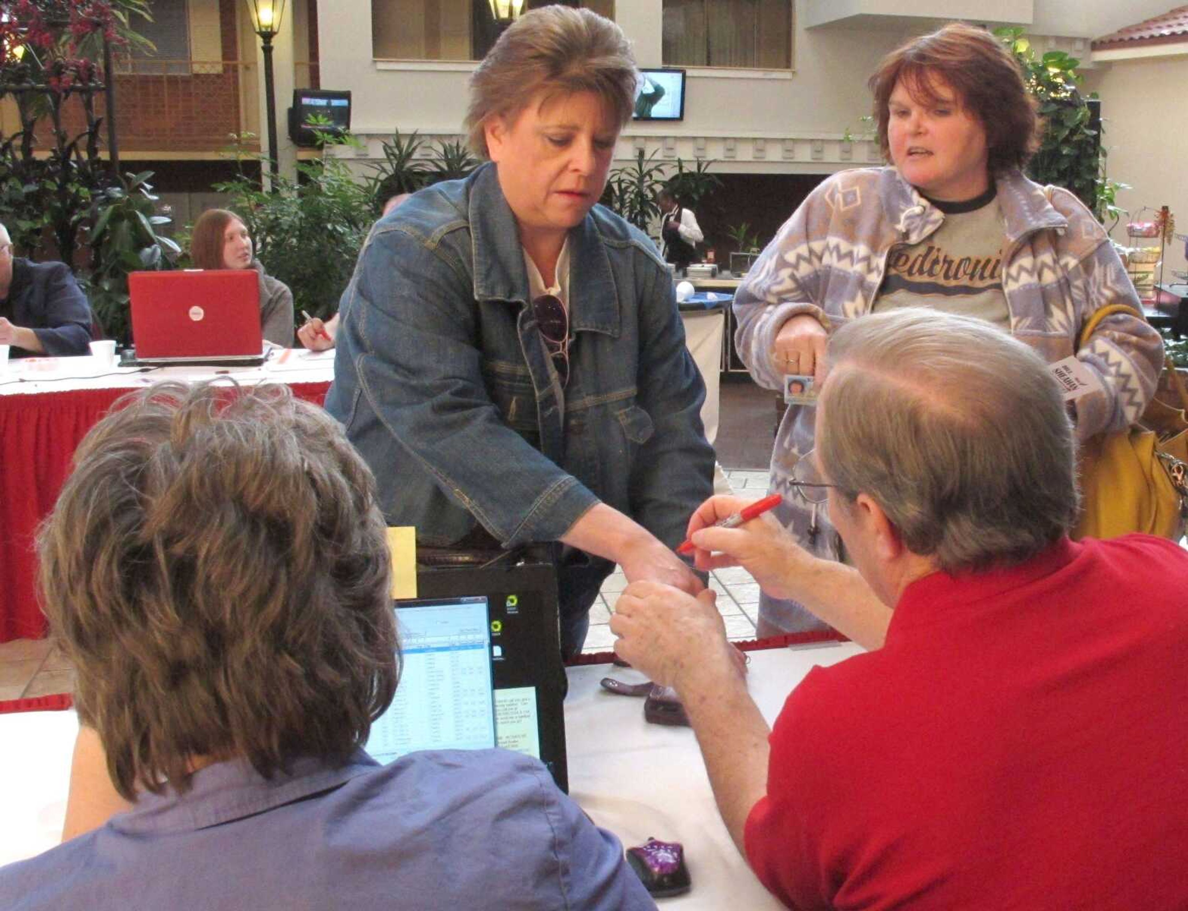 Roberta Currie, left, a 48-year-old hospital worker from Topeka, gets her hand marked by election workers Saturday to show that she can vote in the Kansas Republican presidential caucuses in Topeka, Kan. To her right, her friend, Mamie Lindberg, of Alma, a 48-year-old unemployed administrative assistant, shows photo identification. (John Hanna ~ Associated Press)