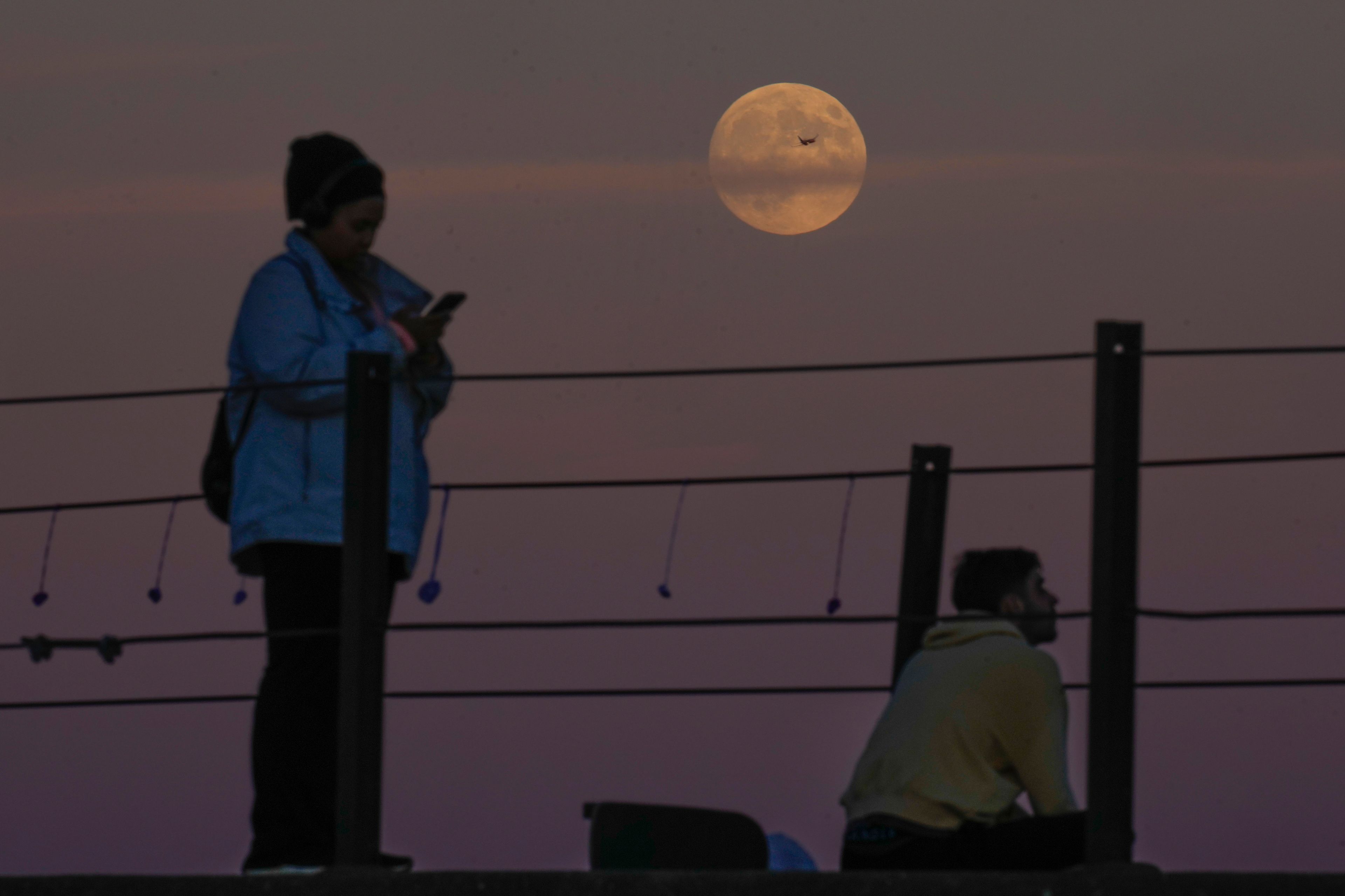 An airplane crosses the supermoon as people watch it rise over Lake Michigan, Wednesday, Oct. 16, 2024, in Chicago. (AP Photo/Erin Hooley)