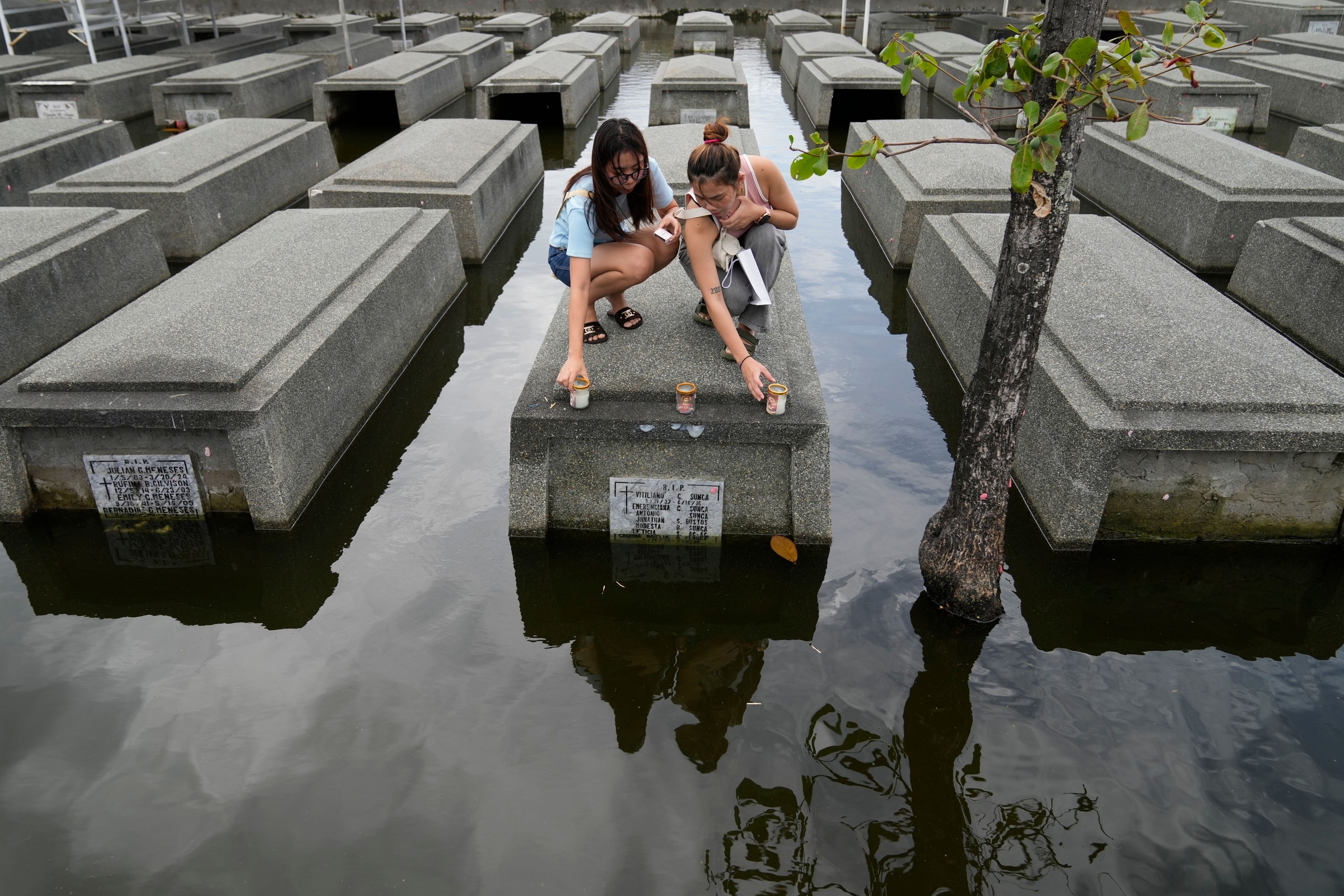 FILE - Women place candles on the half-submerged tomb of family members at flood-prone Holy Spirit Memorial Park in Masantol, Pampanga province, Philippines after heavy rains from recent tropical storm Trami caused water to become higher than usual, ahead of All Saints Day, Oct. 31, 2024. (AP Photo/Aaron Favila, File)