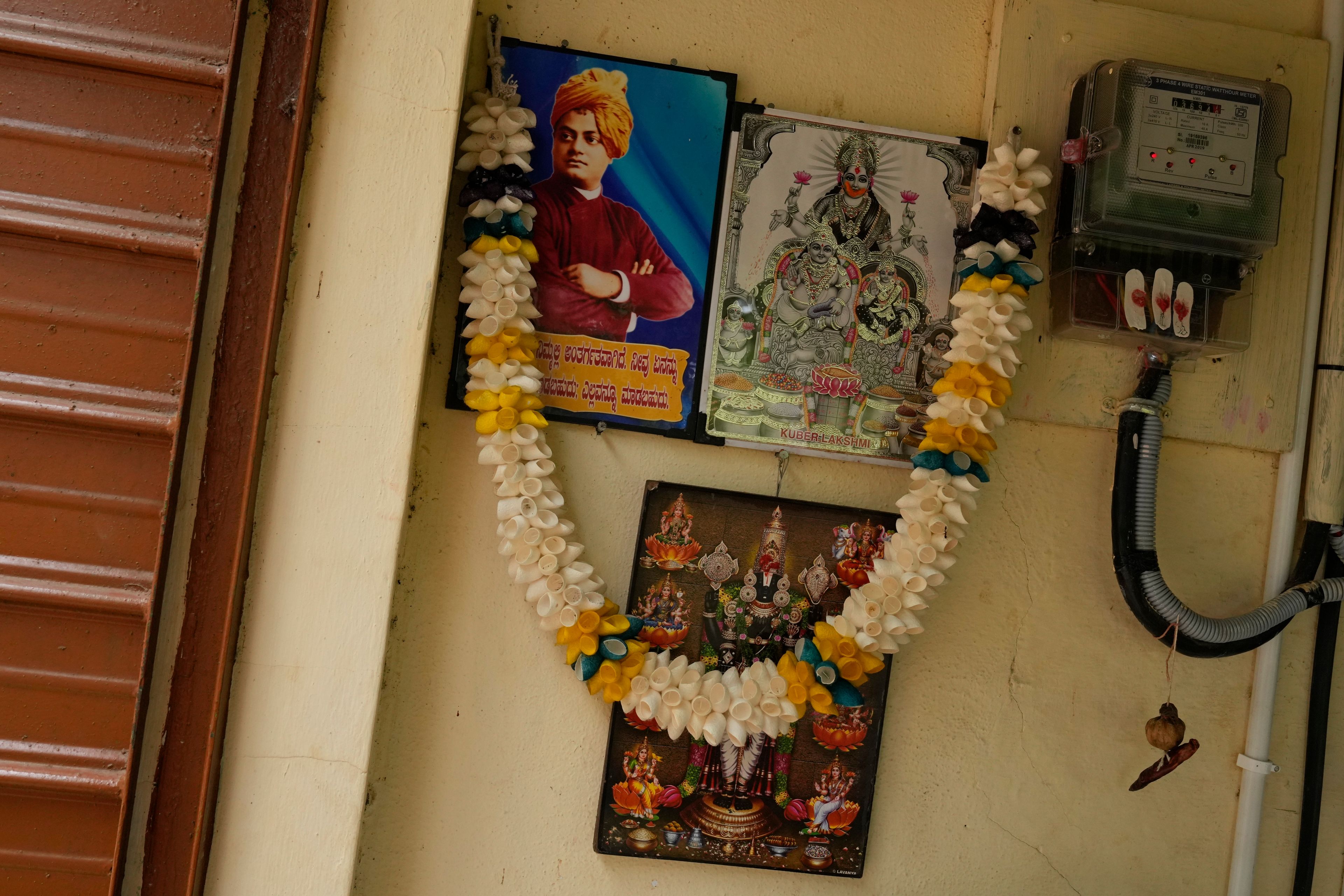 Pictures of Indian scholar Swami Vivekananda, left, and Hindu goddesses are displayed next to an electric meter inside a small garage where a group of tailors use electric sewing machines to stitch clothes, at the campus of the Swami Vivekananda Youth Movement, a nongovernmental organization that works to help poor and Indigenous communities, in Kenchanahalli, India, Monday, Sept. 23, 2024. (AP Photo/Aijaz Rahi)