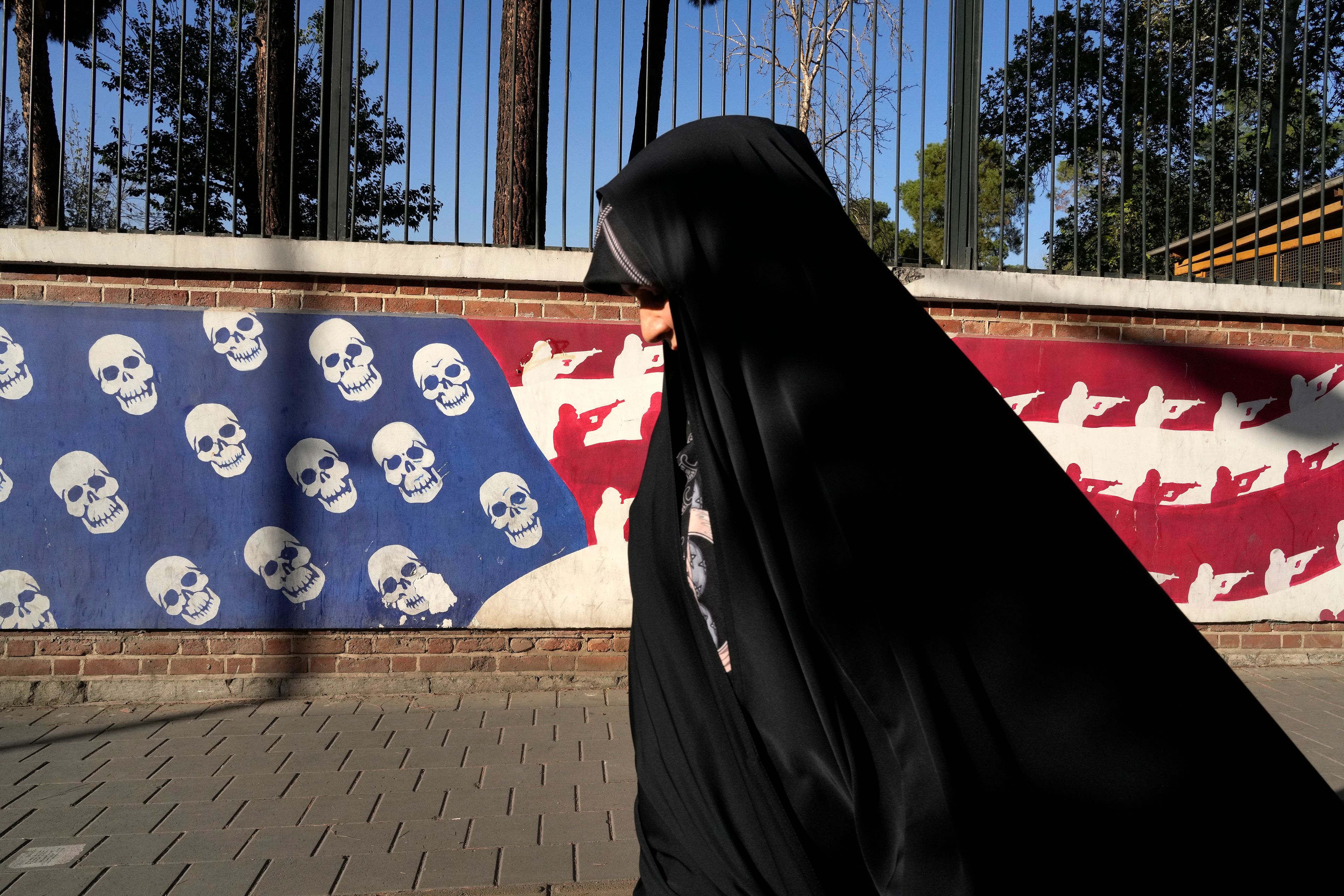 An Iranian woman walks past a satirised image of the U.S. flag on the wall of former U.S. embassy, in Tehran, Iran, Tuesday, Oct. 22, 2024. (AP Photo/Vahid Salemi)