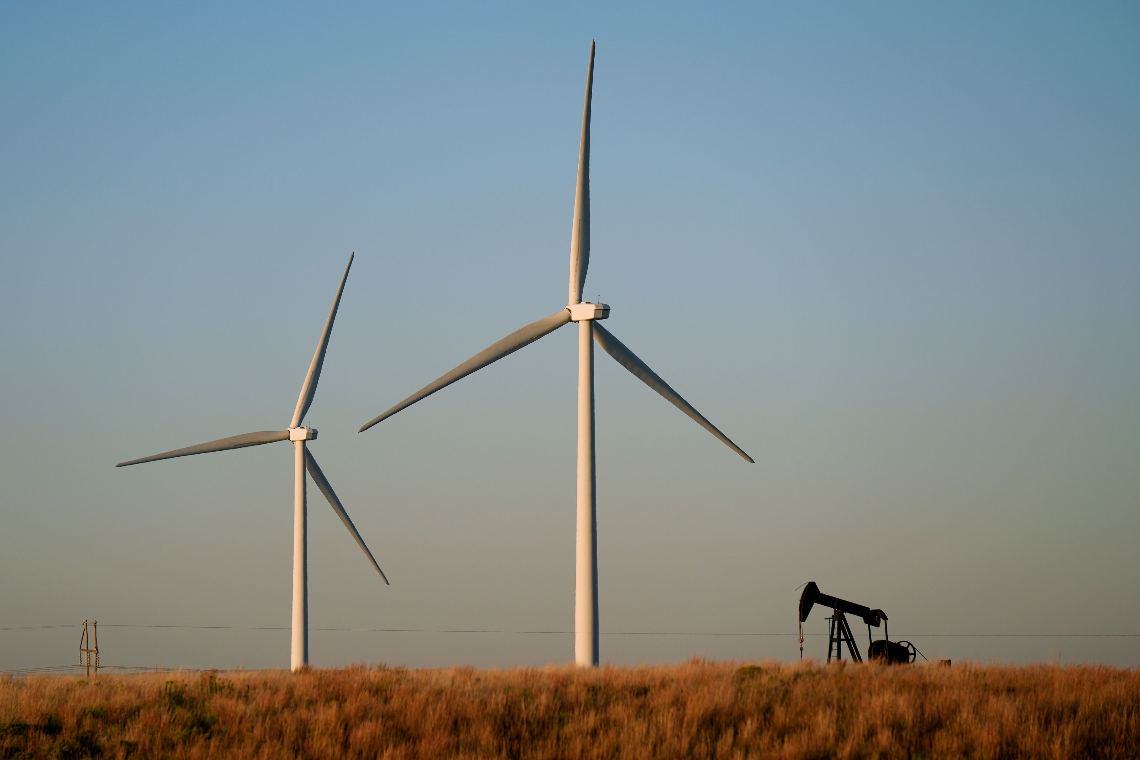 A pumpjack operates in the foreground while a wind turbine at the Buckeye Wind Energy wind farm rises in the distance, Monday, Sept. 30, 2024, near Hays, Kan. (AP Photo/Charlie Riedel)