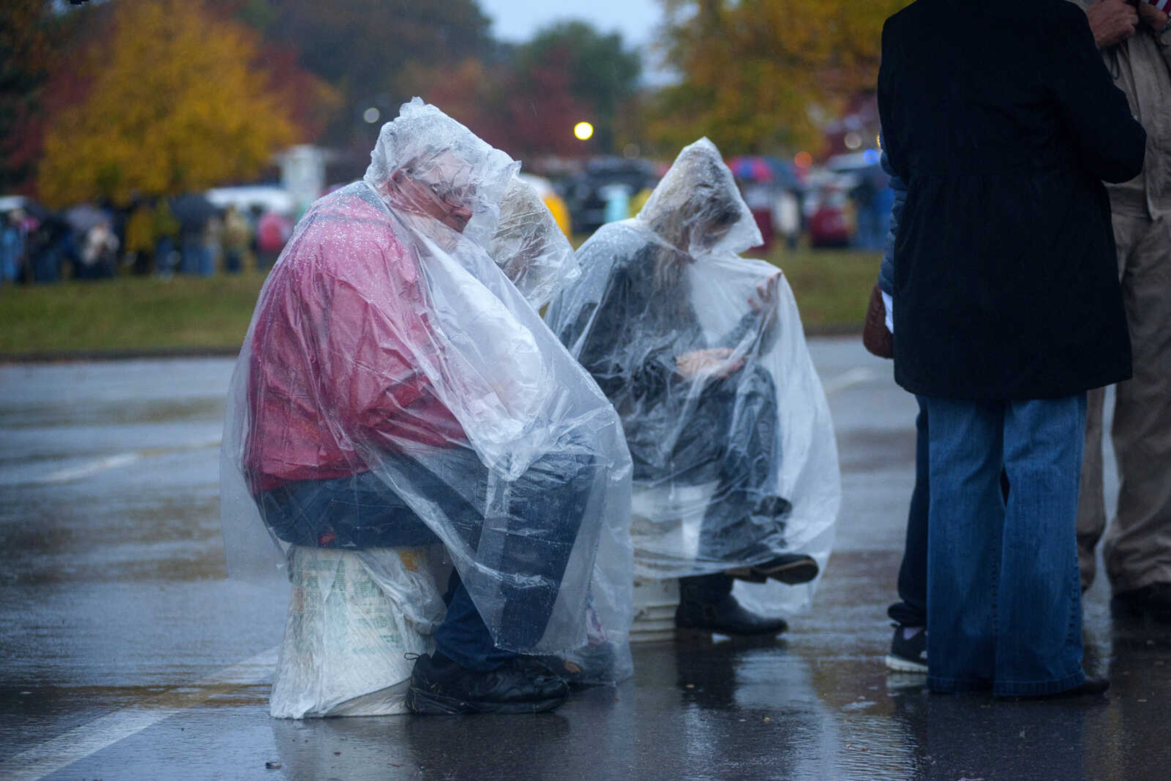 Ticket-holders wearing ponchos sit in the rain while waiting to enter Show Me Center for a Make America Great Again rally Monday, Nov. 5, 2018.