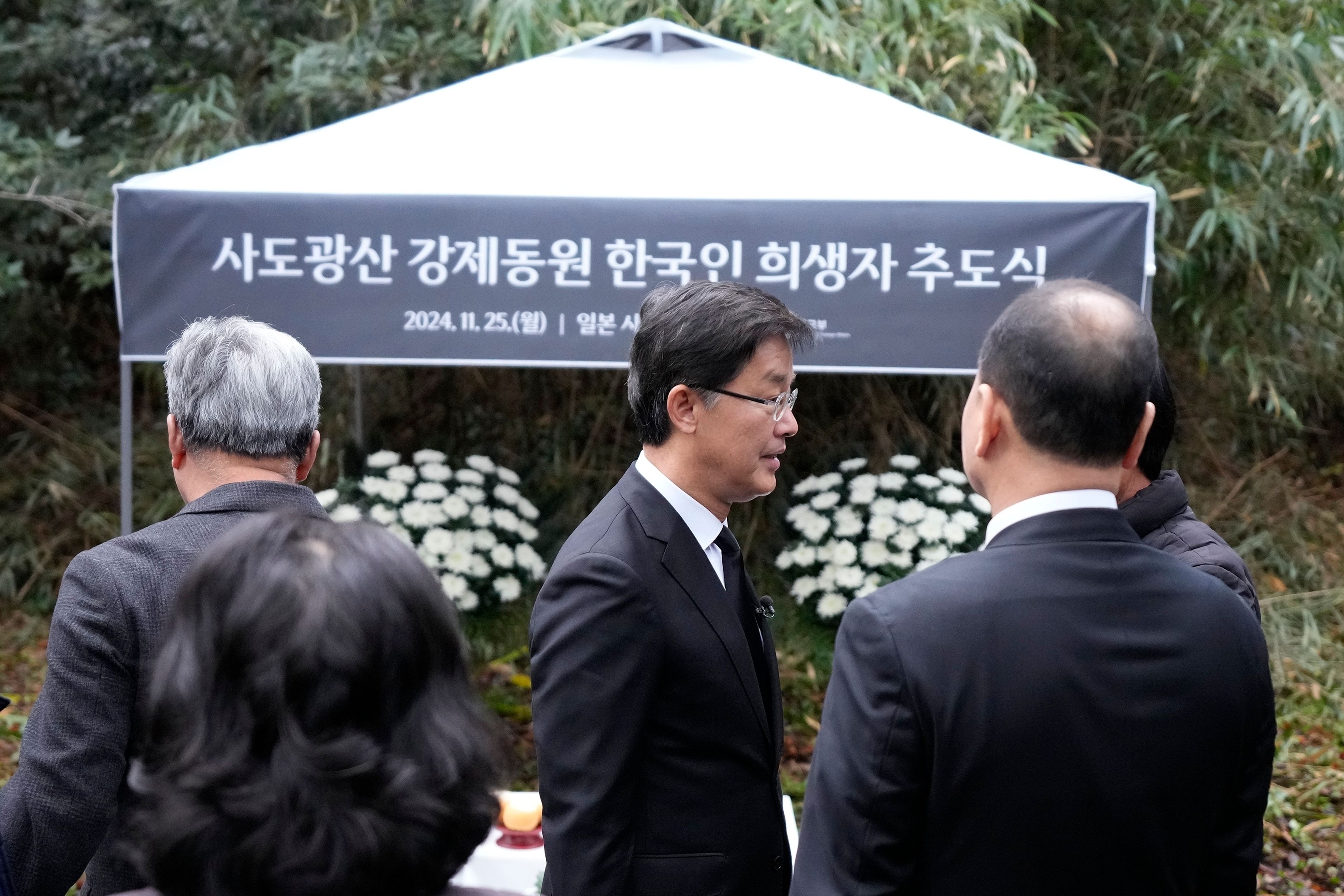 South Korean Ambassador to Japan Park Cheol-hee, center, speaks with the relatives of Korean victims and South Korean officials at the site of former Fourth Souai Dormitory for the mine workers from the Korean Peninsula, after a memorial service in Sado, Niigata prefecture, Japan, Monday, Nov. 25, 2024, a day after boycotting a memorial organized by Japanese officials. The black banner reads "A memorial service for Korean forced laborer victims at Sado Mine." (AP Photo/Eugene Hoshiko)