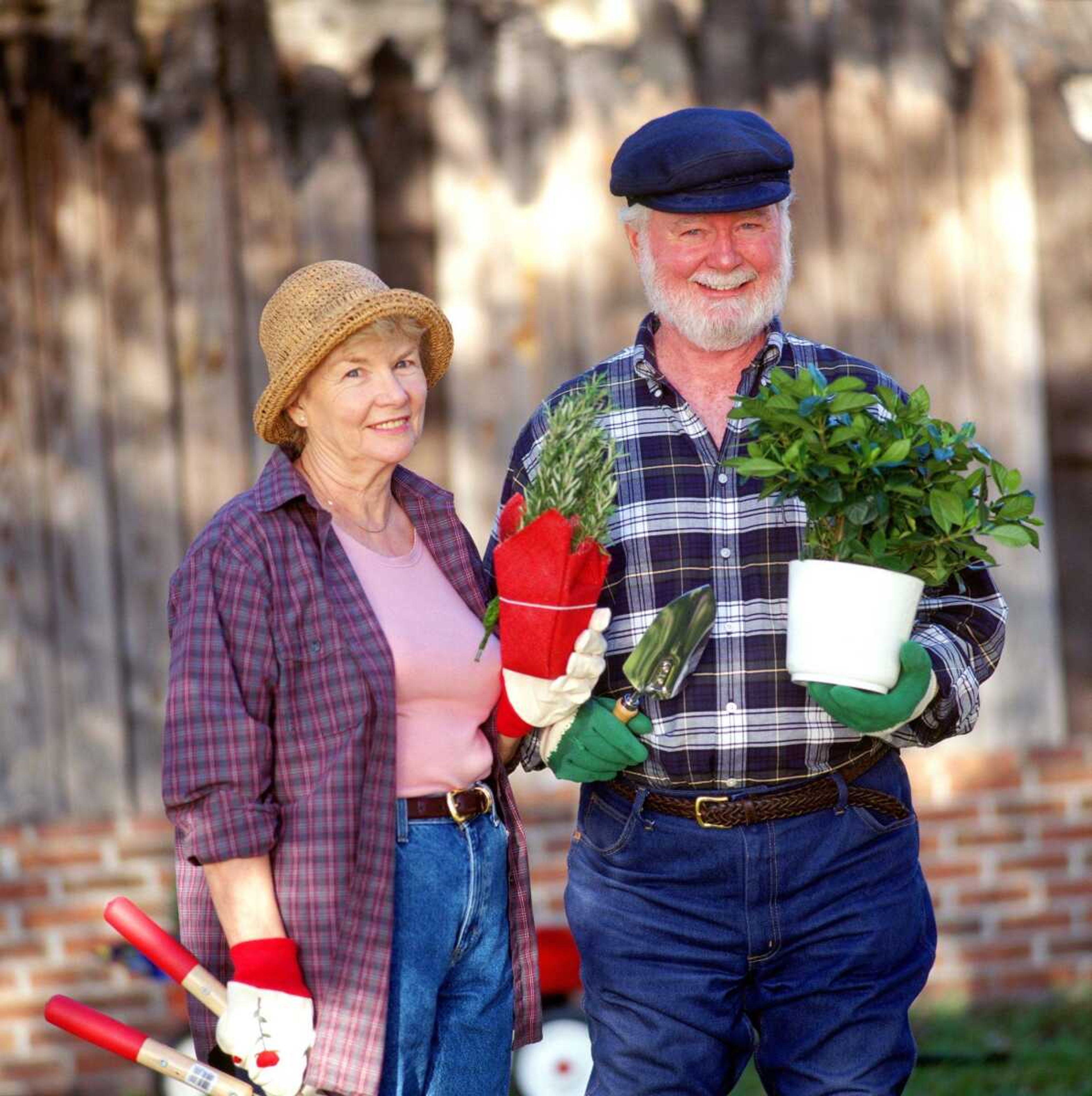 portrait of a mature couple holding plants and wearing gardening attire