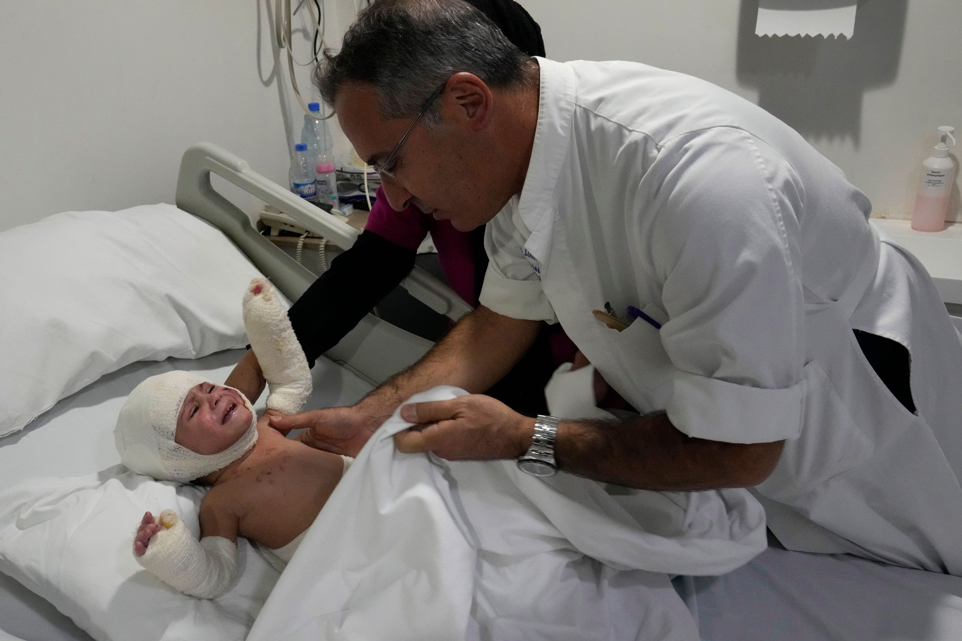 Plastic surgeon doctor Ziad Sleiman, inspects Ivana Skakye, 2, a Lebanese child who is suffering from third-degree burns over 40 percent of her body following an Israeli airstrike last September near their home in Deir Qanoun al Nahr a village in south Lebanon, as she lies on a bed at the Geitaoui hospital where she is receiving treatment, in Beirut, Lebanon, Tuesday, Oct. 29, 2024. (AP Photo/Hussein Malla)