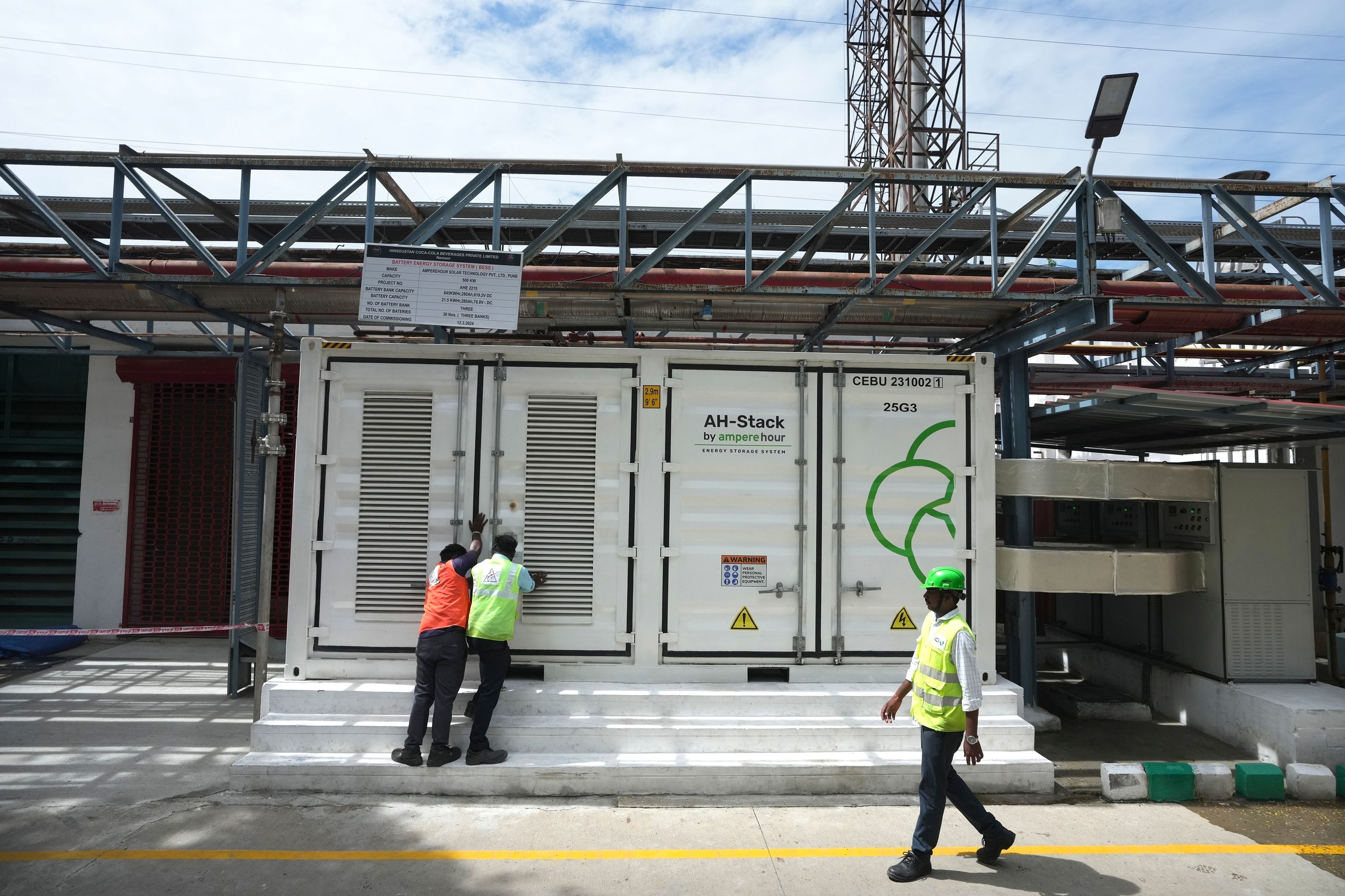 FILE - Team leader K. Sridhar, center, closes the doors after a routine check of lithium-ion batteries of 500-kilowatt battery energy storage system inside the Hindustan Coca-Cola Beverages factory in Thiruvallur District, on the outskirts of Chennai, India, Tuesday, July16, 2024. (AP Photo/Mahesh Kumar A., File)