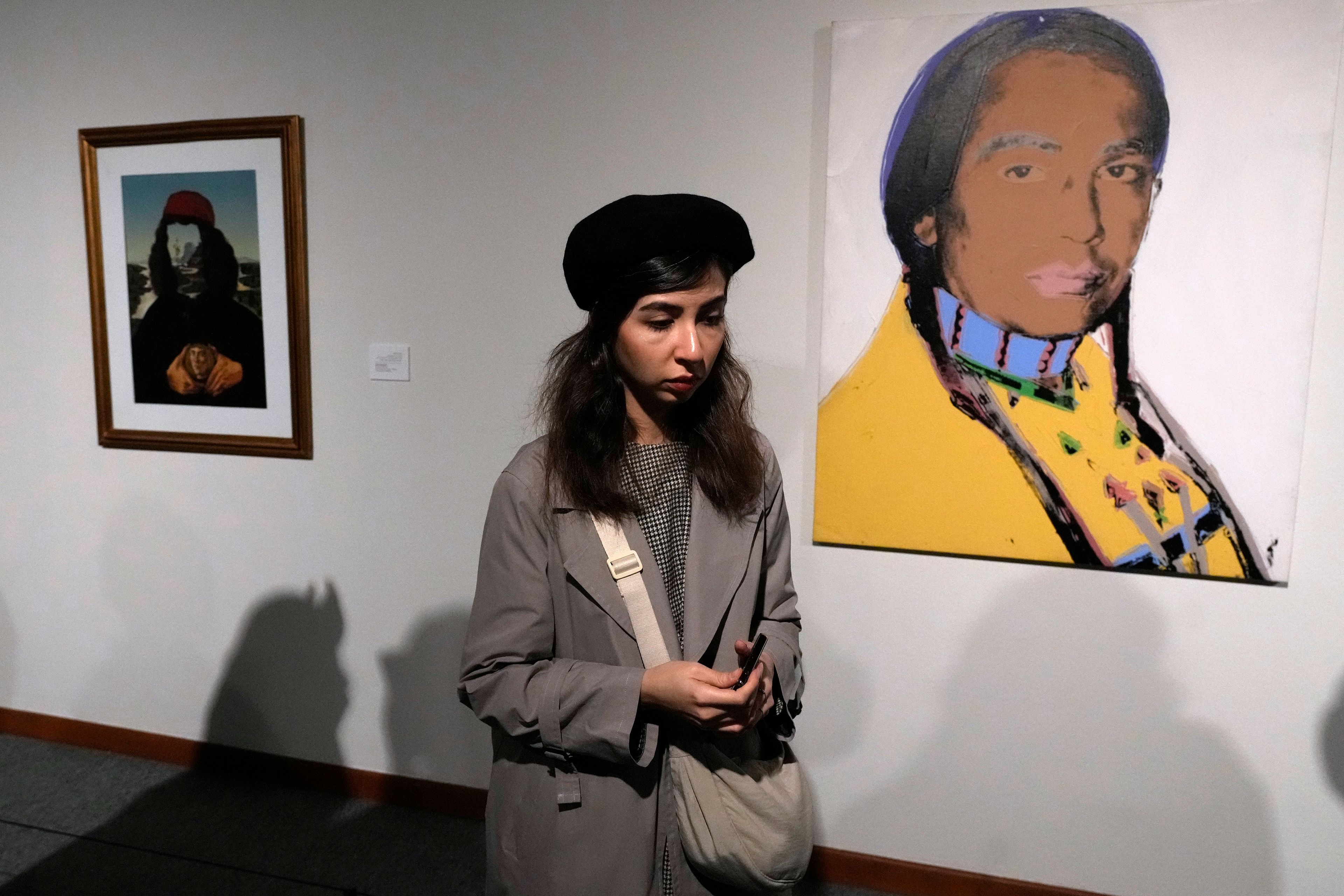 A woman walks past a portrait of the leader of the American Indian Movement Russell Means, right, by American artist Andy Warhol, as she visits an exhibition titled Eye to Eye which showcases over 120 works by modern world artists as well as Iranian painters at Tehran Museum of Contemporary Art, in Tehran, Thursday, Nov. 21, 2024. (AP Photo/Vahid Salemi)