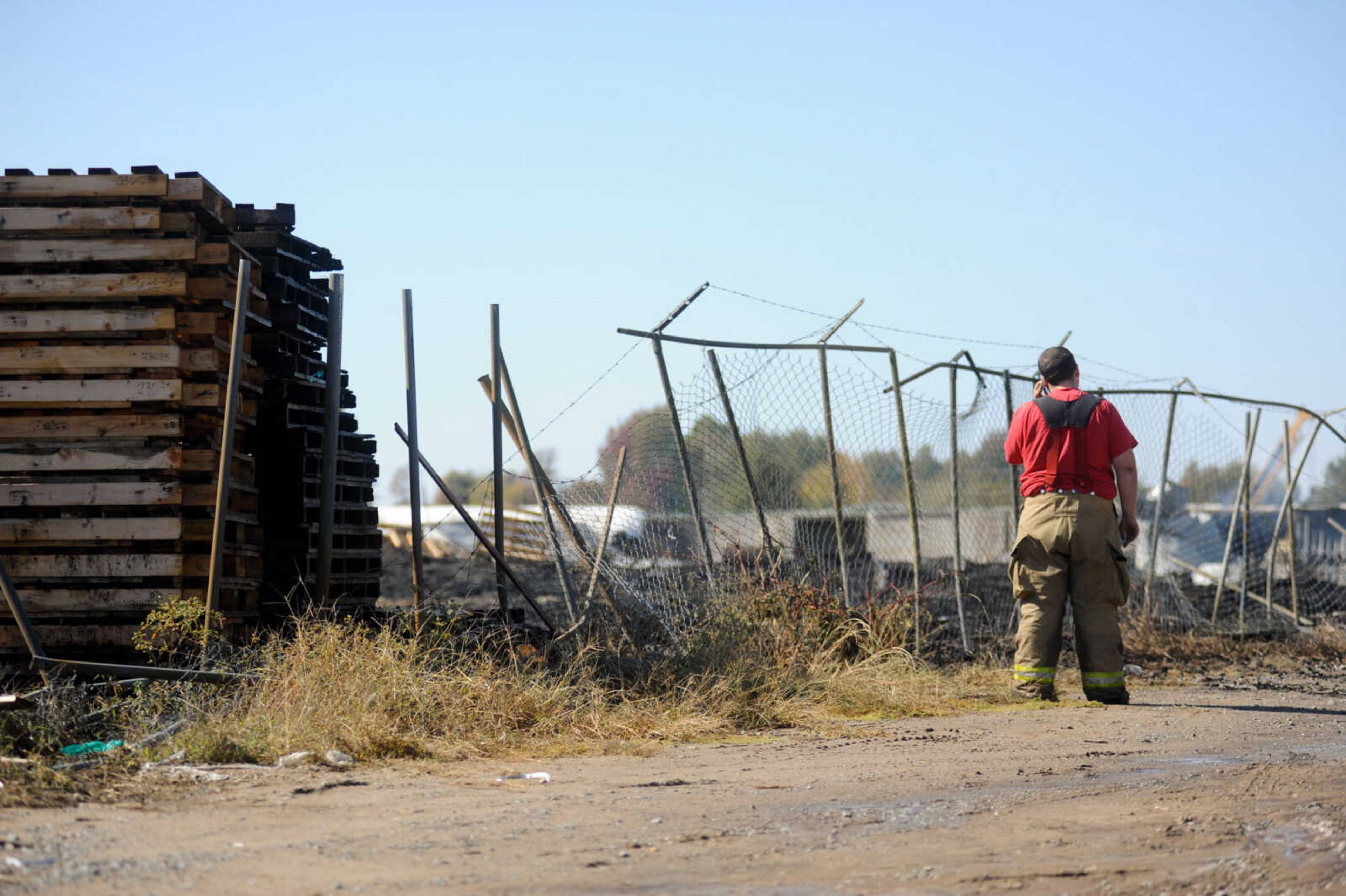 Justin Gordon with the Scott County Rural Fire Protection District takes a phone call after spraying water on smoldering pallets Wednesday, Oct. 21, 2015 after a fire broke out at Pallet Connection on Route H in Scott County early Wednesday morning. (Glenn Landberg)