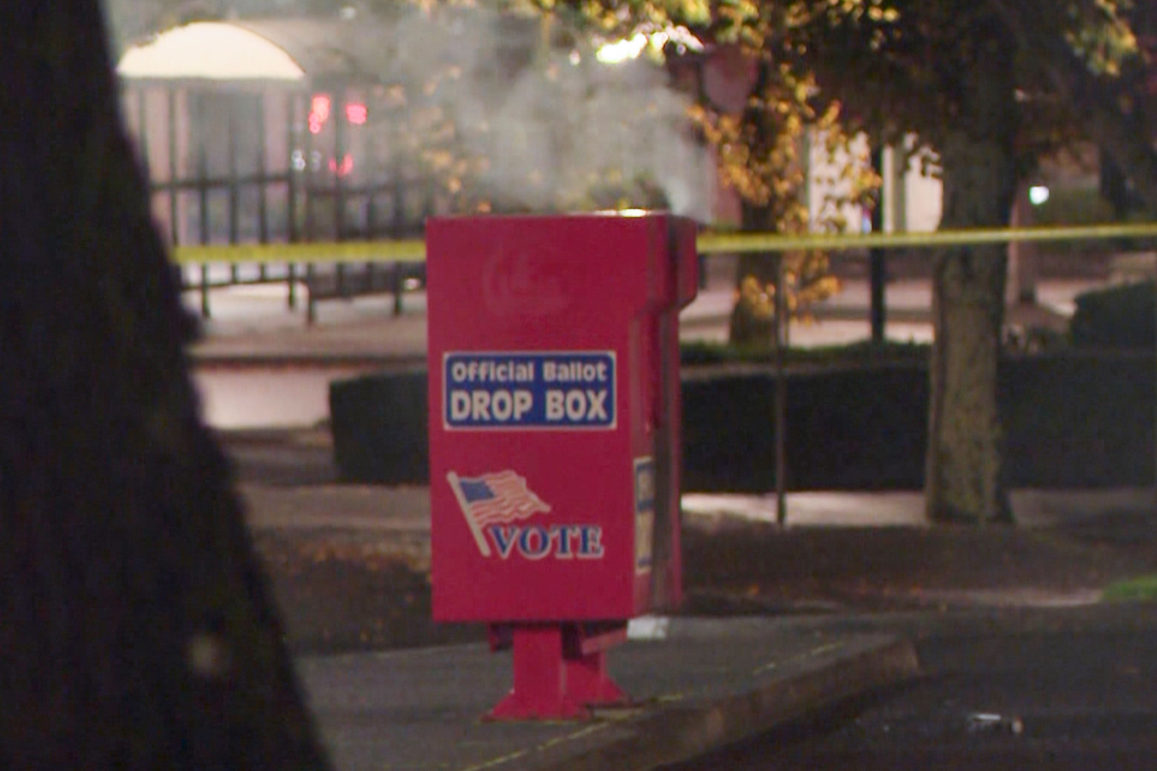 In this image made from a video provided by KGW8, authorities investigate the scene as smoke pours out of a ballot box on Monday, Oct. 28, 2024, in Vancouver, Wash. (KGW8 via AP)