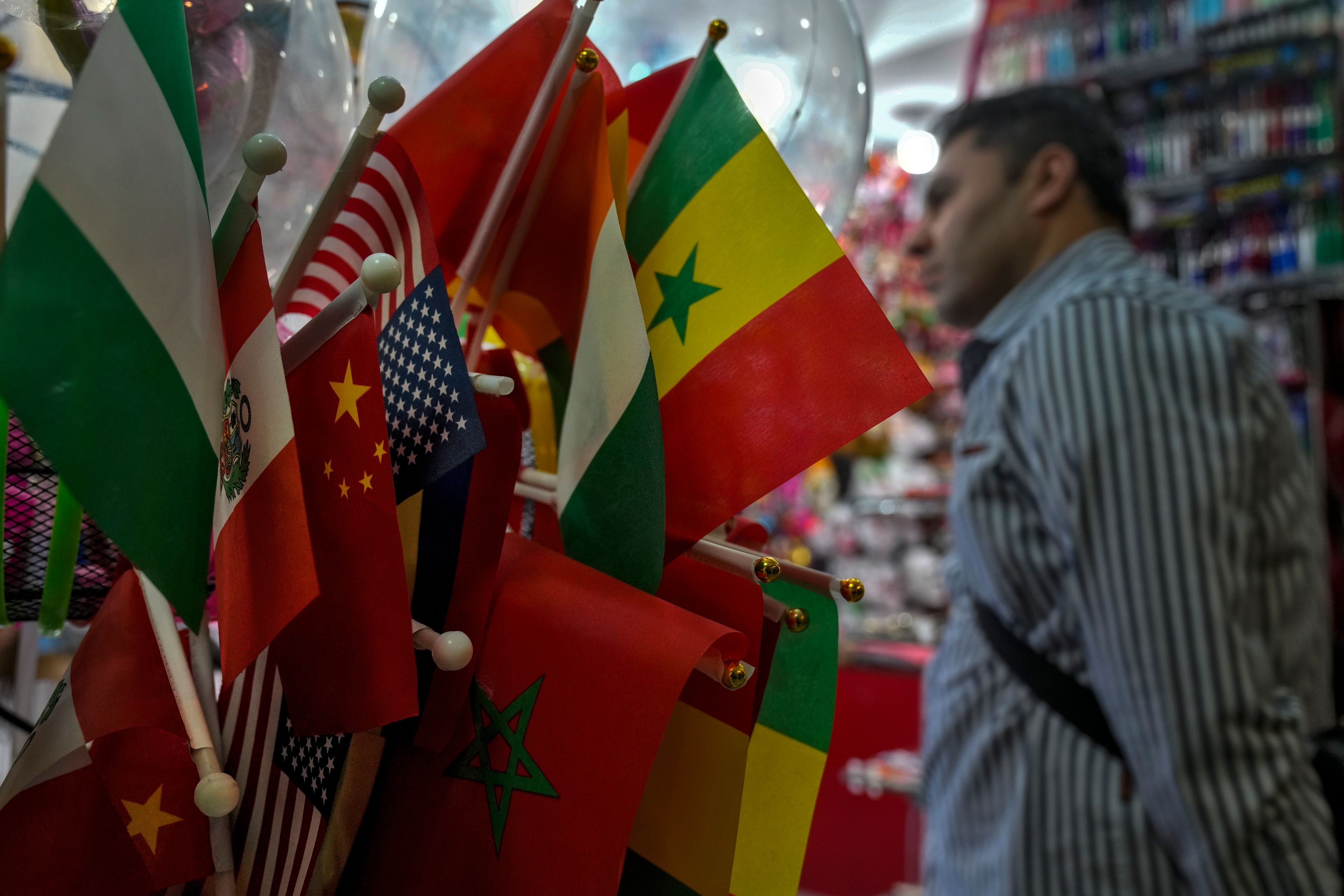 A foreigner walks by flags on display at a stationery store at the Yiwu wholesale market in Yiwu, east China's Zhejiang province on Nov. 8, 2024. (AP Photo/Andy Wong)