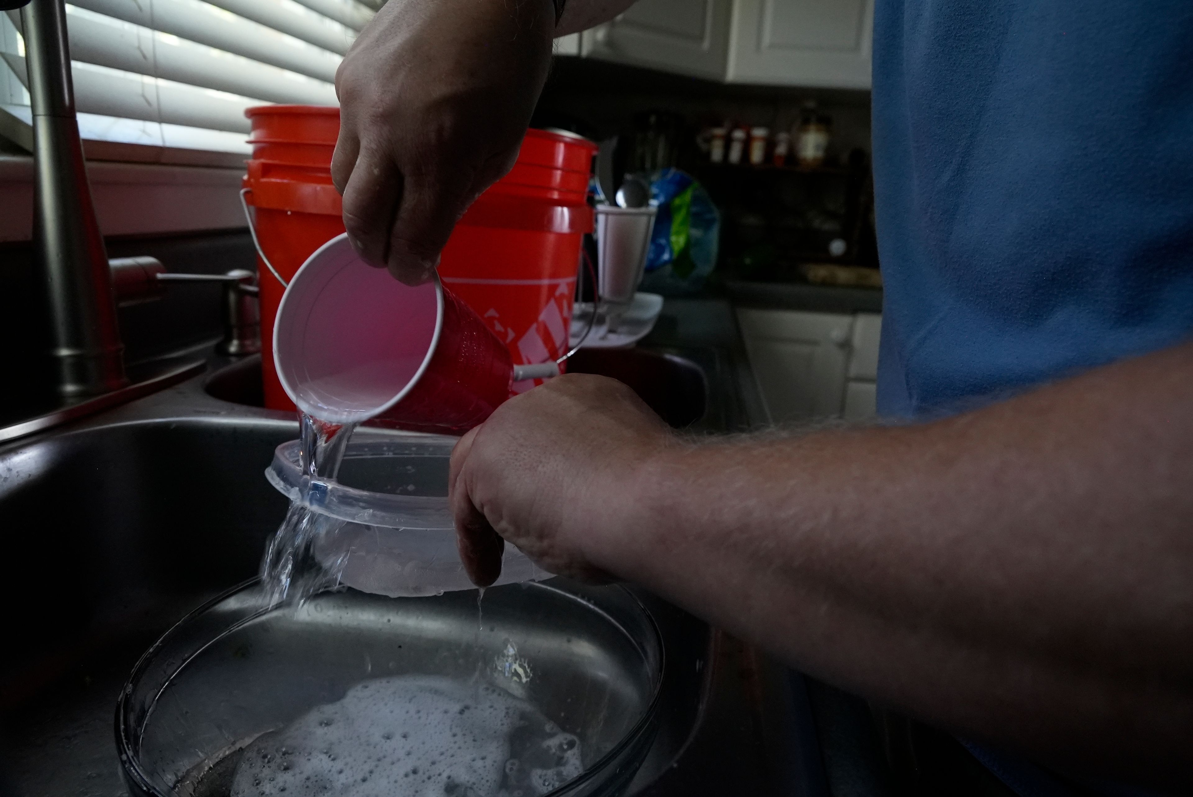 Travis Edwards captures excess water while cleaning dishes Thursday, Oct. 3, 2024 in Asheville, North Carolina. He hasn't had water since Hurricane Helene struck the area, and reuses water to flush toilets. (AP Photo/Brittany Peterson)