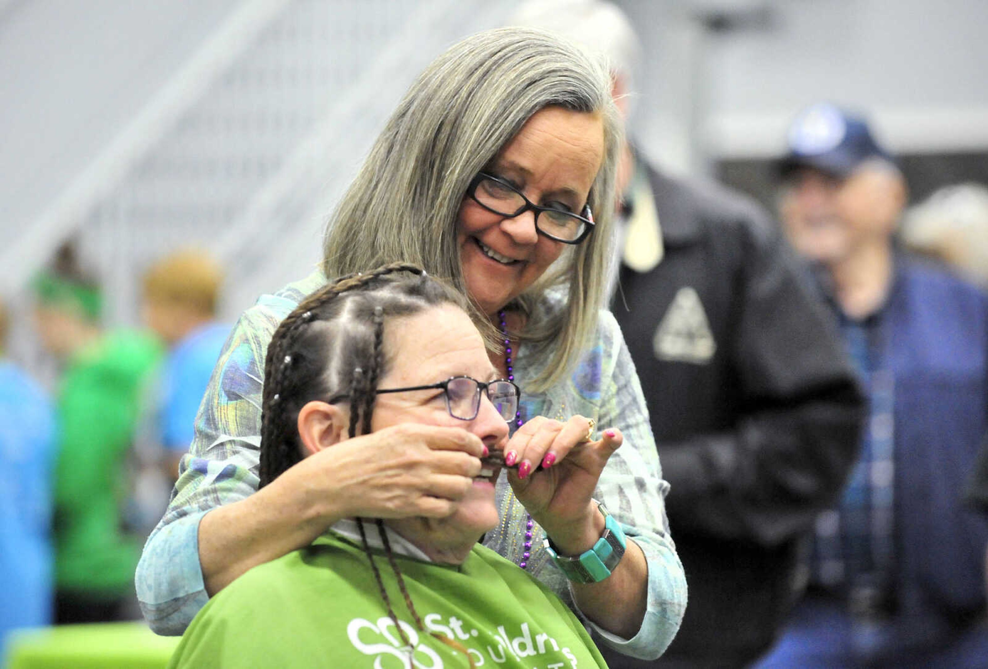 Liz Martin holds up one of Cathy Klaus' braids to her upper lip to make a mustache on Saturday, March 4, 2017, during the St. Baldrick's Foundation fundraiser at Old Orchard CrossFit in Jackson.