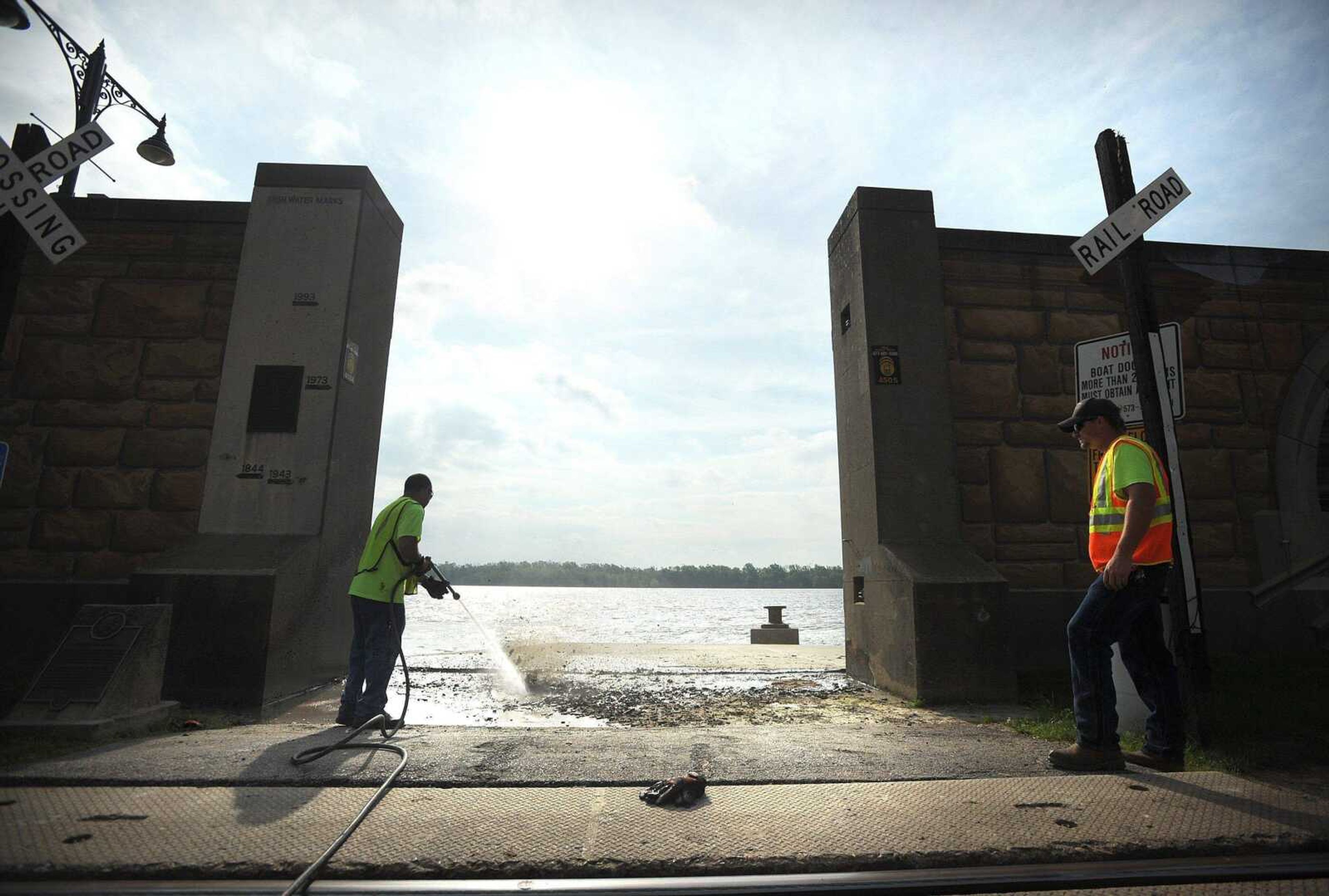 Chuck Hebrosk with the Cape Girardeau Public Works department sewer maintenance division, right, watches his co-worker Jeff Golden use a pressure washer to clear mud from the Themis Street floodwall entrance May 20, 2013. The flood gates had been closed since April 19, 2013, as the Mississippi River rose to flood stage. (Laura Simon)