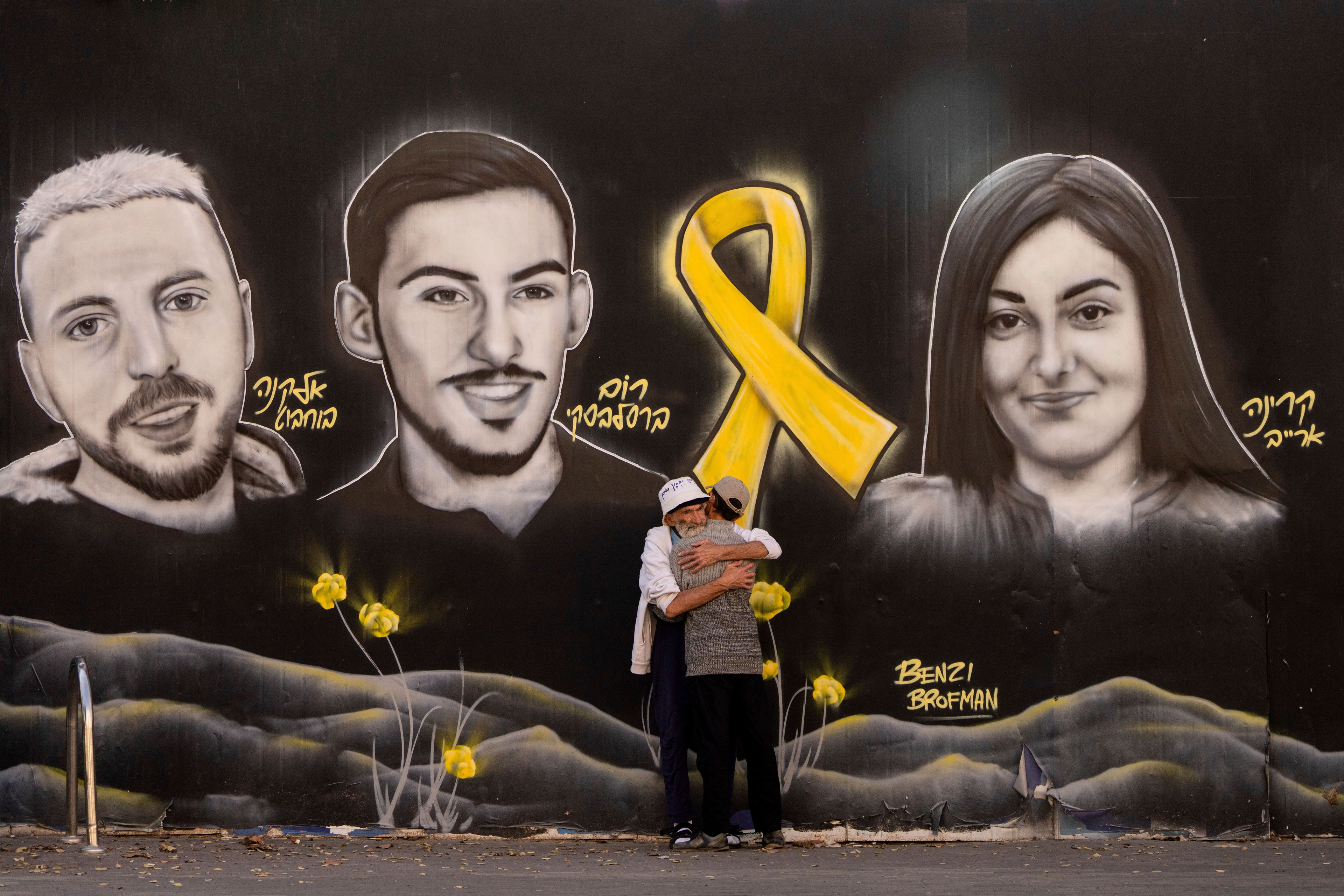 People hug next to graffiti portraits of Gaza-held hostages in Jerusalem, Friday, Nov. 22, 2024. (AP Photo/Ohad Zwigenberg)