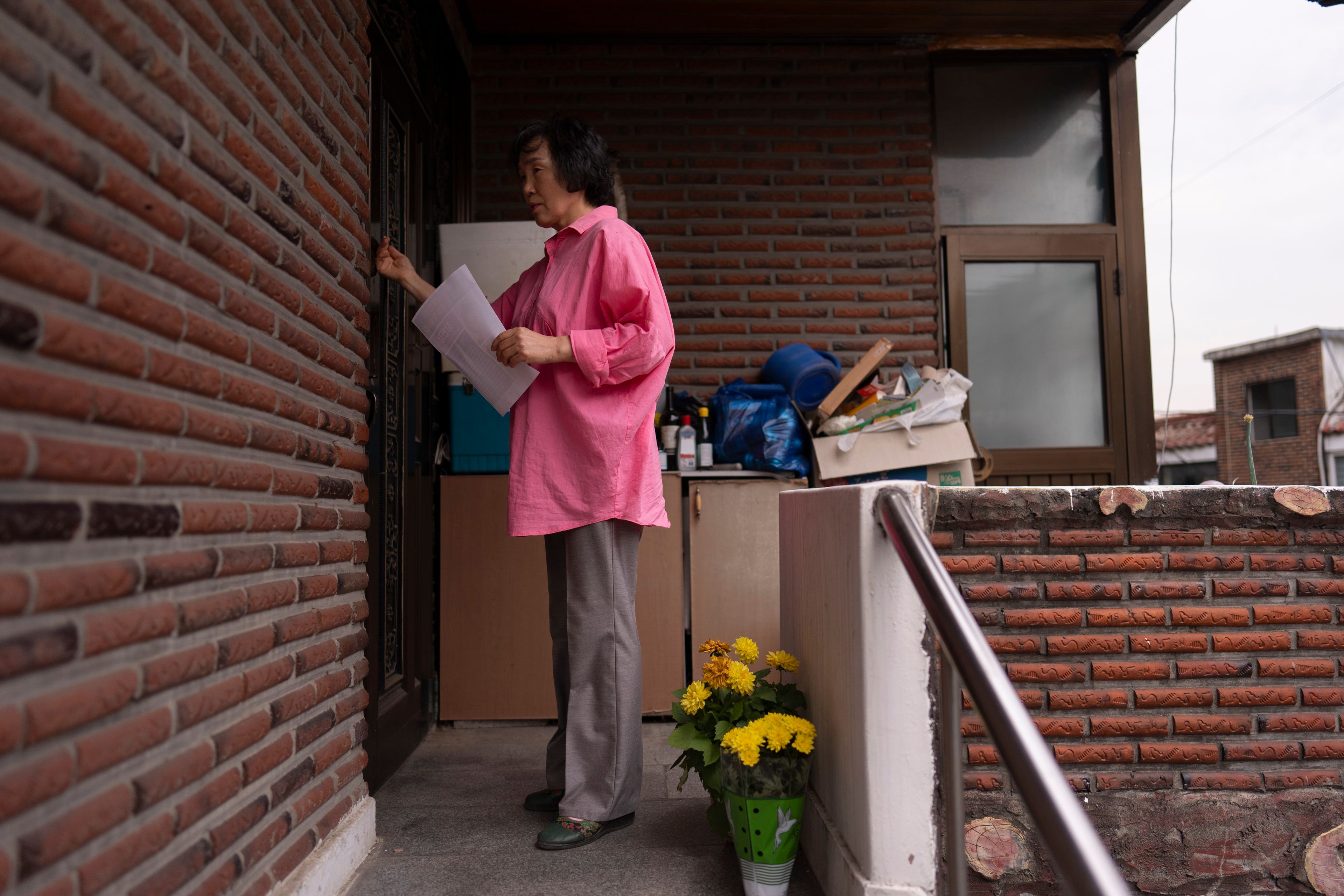 Holding a flyer asking for help to find adoptee Nicole Motta's birth family, long-time resident An Bok-rye knocks on the door of an apartment building where Motta's home once stood in Bucheon, South Korea, Thursday, May 30, 2024. Sympathetic residents, police officers and city workers of the towns where they once lived often try to assist adoptees searching for their origin story. (AP Photo/Jae C. Hong)