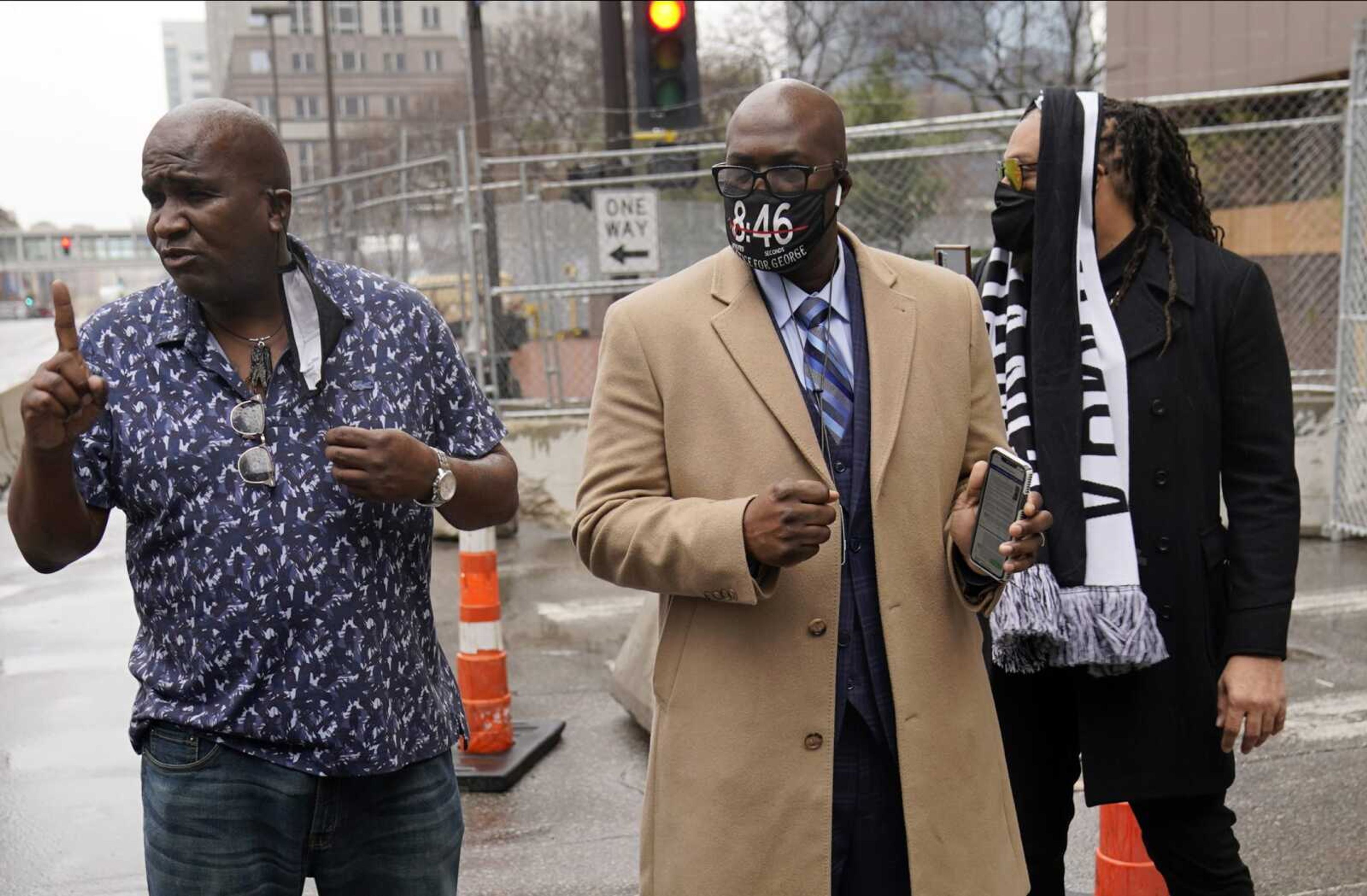 A family security personnel, left, talks to a reporter Friday as Philonise Floyd, brother of George Floyd, listens as Floyd family members arrive at the Hennepin County Government Center in Minneapolis where testimony continues in the trial of former Minneapolis police officer Derek Chauvin. Chauvin is charged with murder in the death of George Floyd during an arrest last May in Minneapolis.