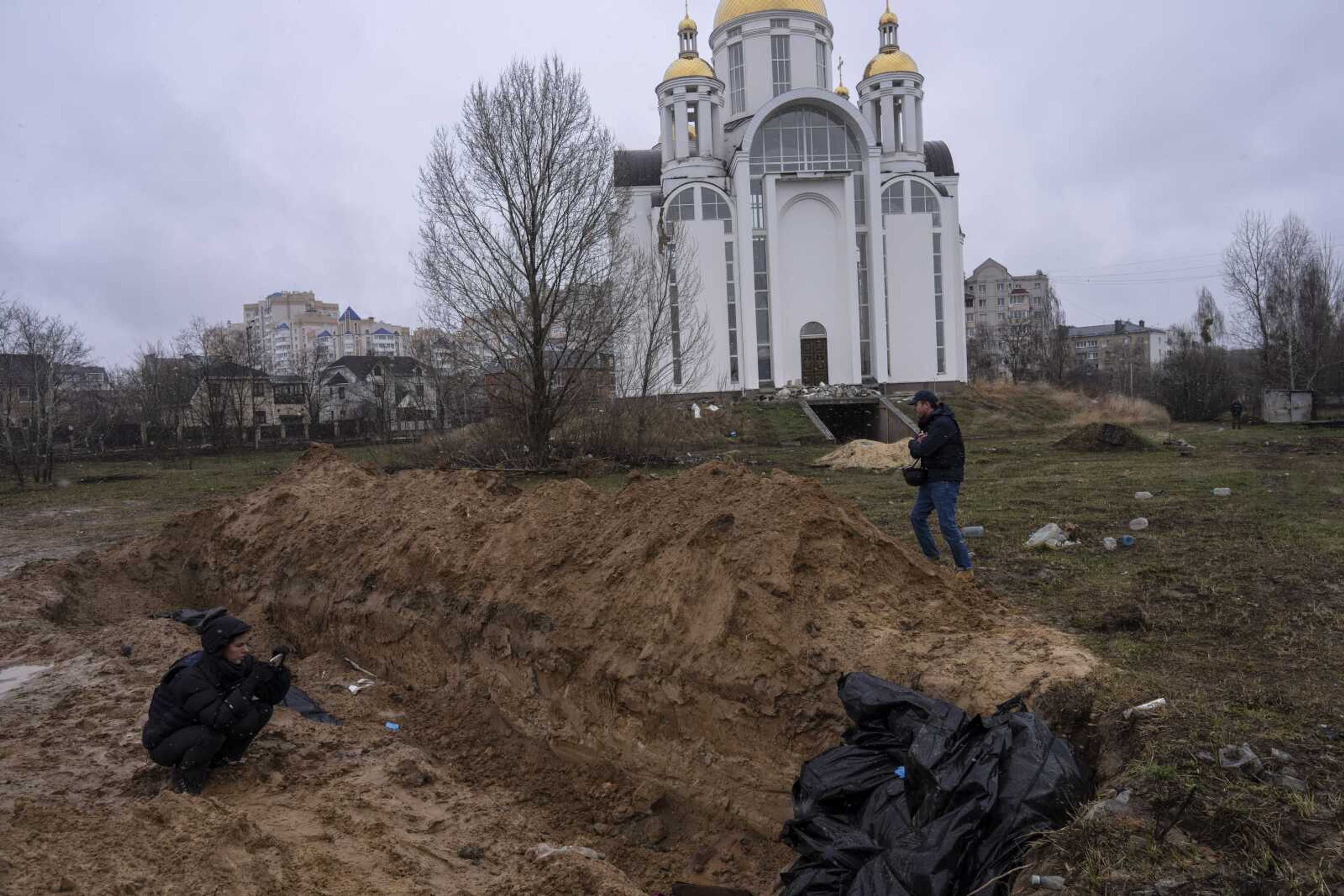 Journalists take pictures next to a mass grave Sunday in Bucha, in the outskirts of Kyiv, Ukraine.