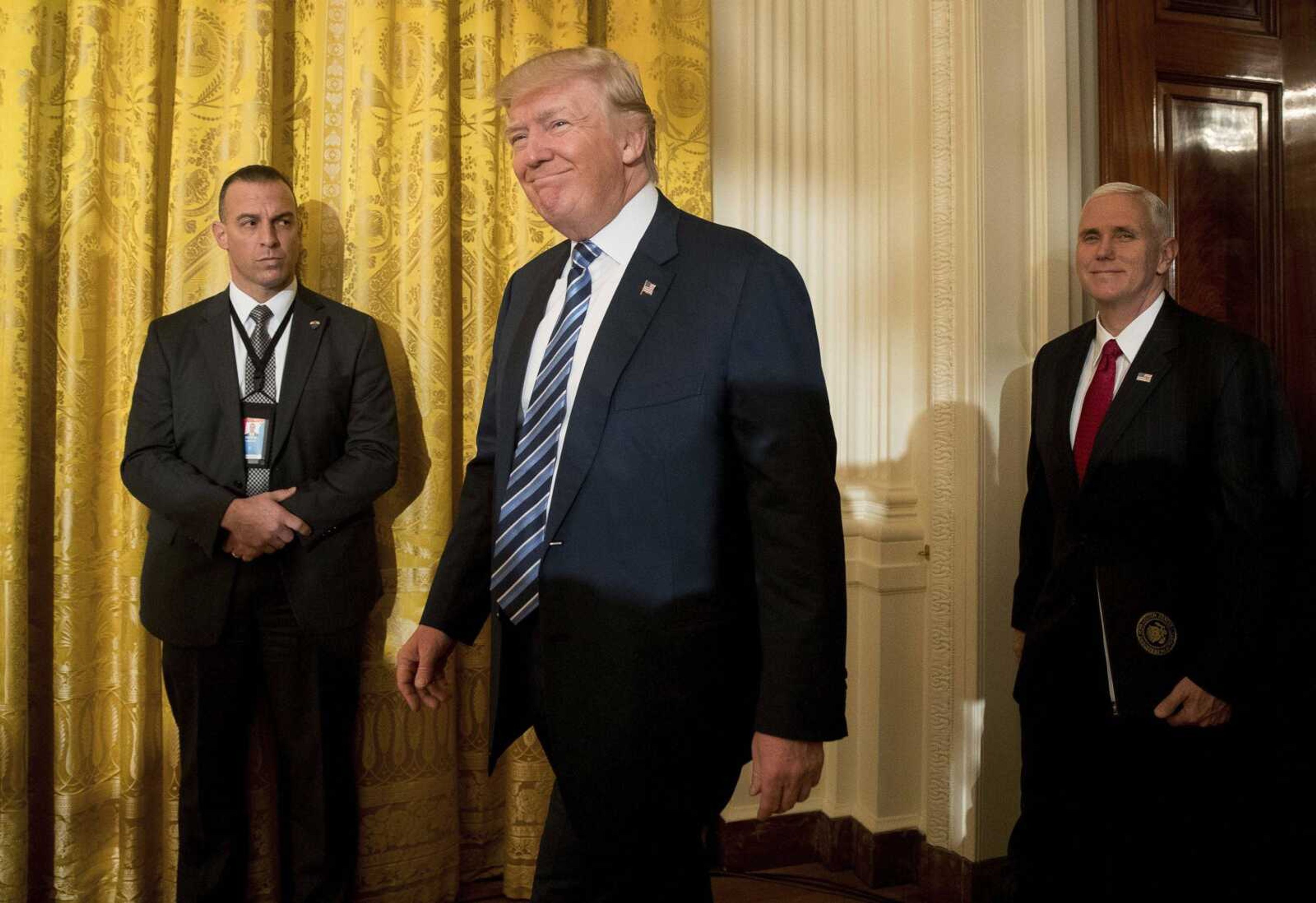 President Donald Trump, center, accompanied by Vice President Mike Pence, right, arrives for a White House senior staff swearing-in ceremony in the East Room of the White House on Sunday in Washington.