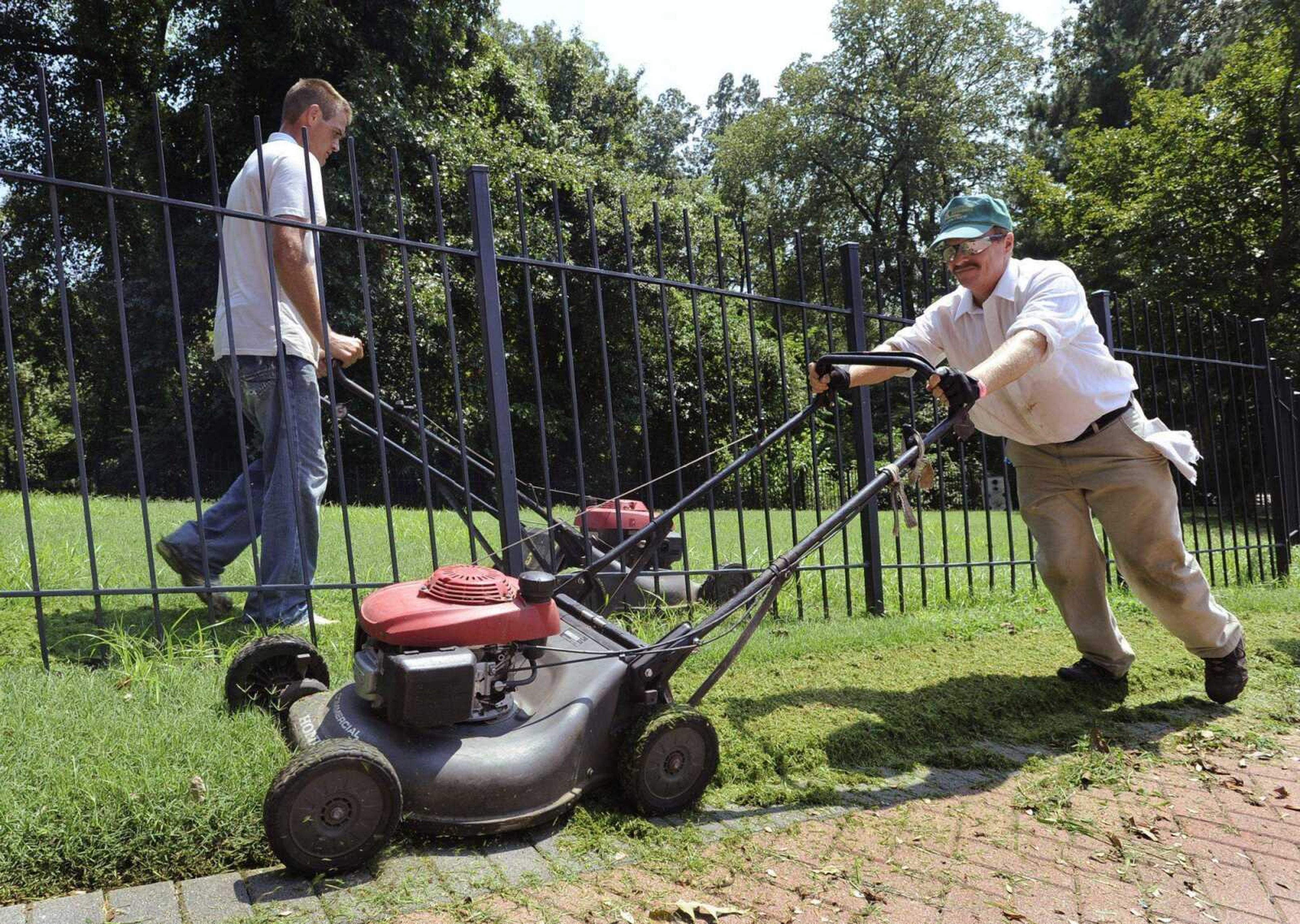 While it's 95 degrees outside, these Teen Challenge students take it in stride. Steve Richardson, right, crosses paths with Randy Willison as they work on a six-man lawn-cutting crew Friday, Aug. 13, 2010 in Cape Girardeau. (Fred Lynch)