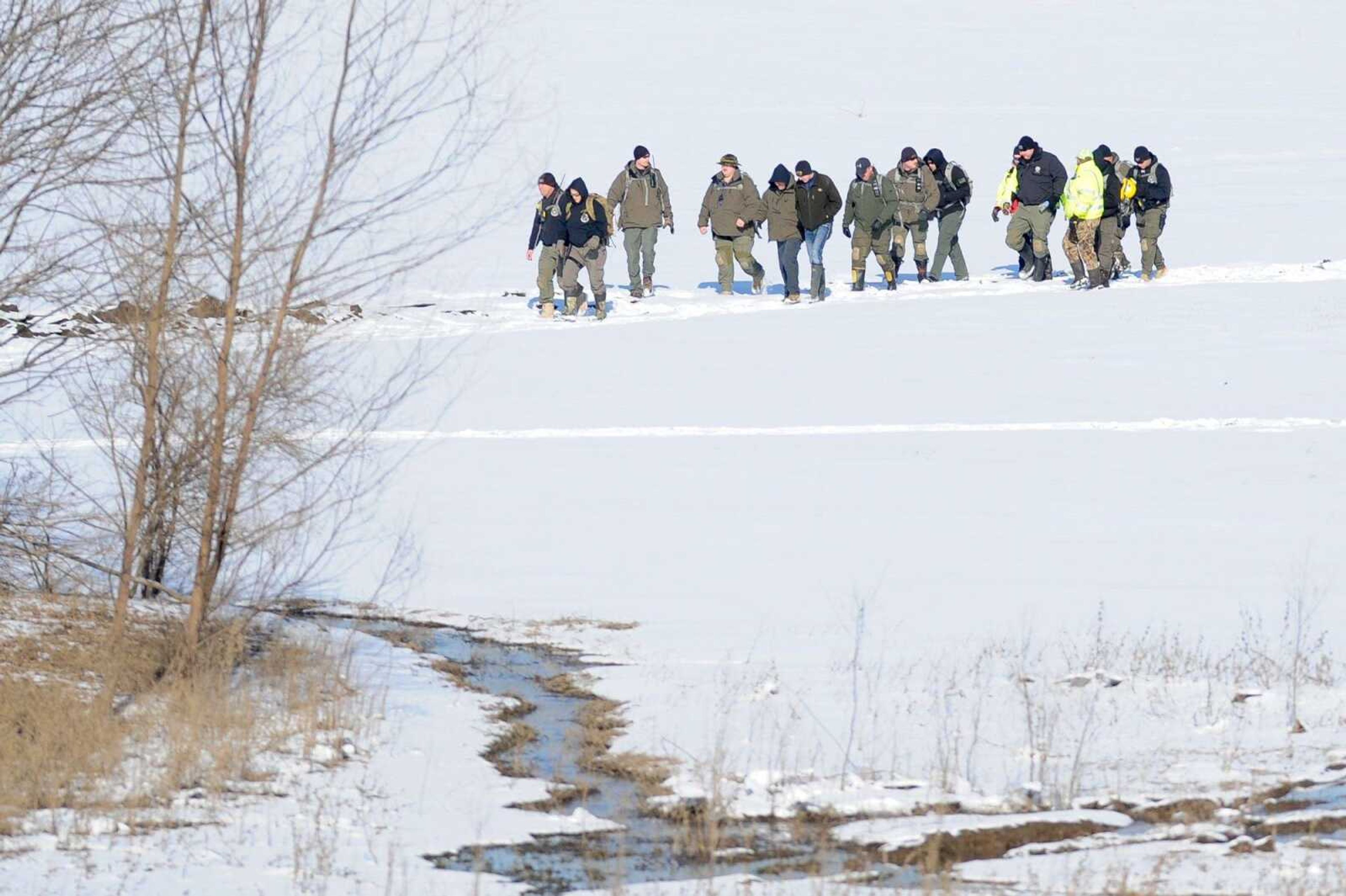 A search crew moves across a snow-covered field Wednesday afternoon looking for missing hunter Zack Johnston. His body later was found submerged in water.