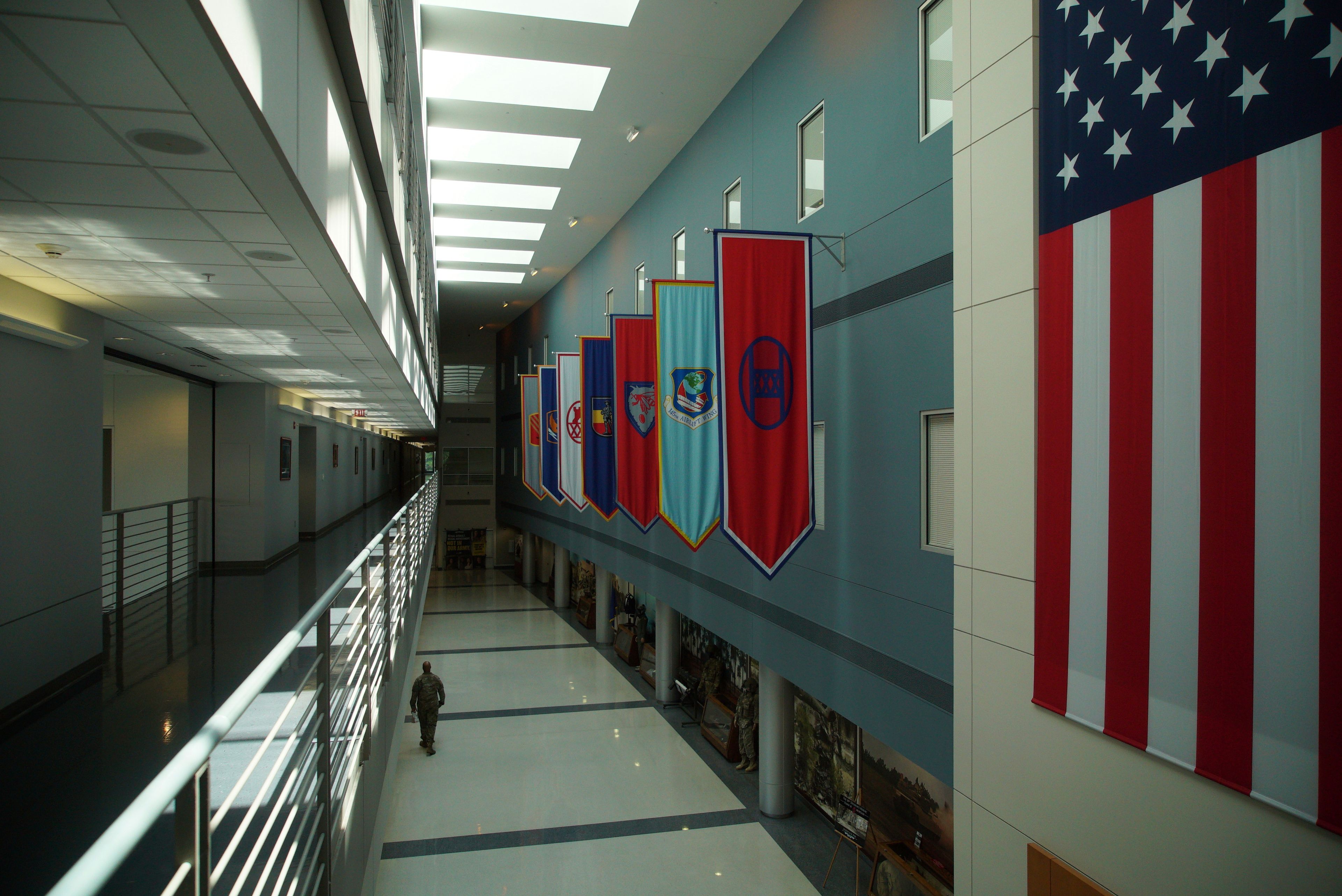 A soldier walks down a hall displaying unit flags at the National Guard headquarters in Raleigh, N.C., on Tuesday, July 30, 2024. Chris Arthur served with the 30th Armored Brigade Combat Team, whose banner is just to the left of the American flag. (AP Photo/Allen G. Breed)