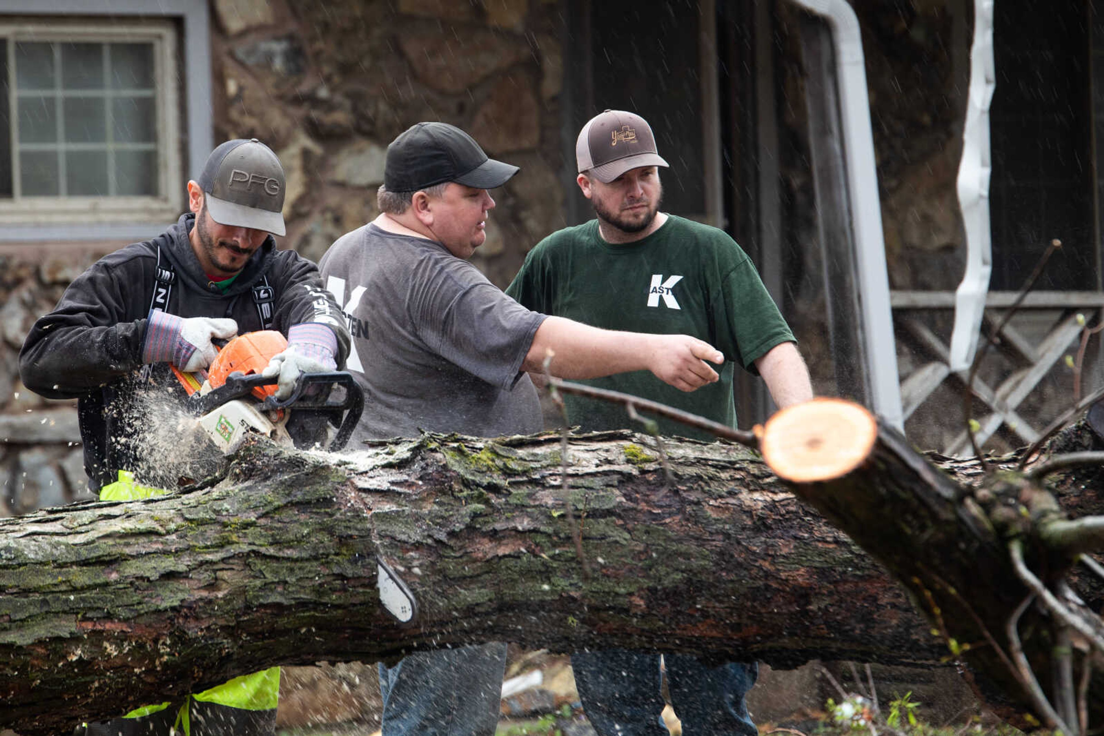 Miguel Echeuarria, left, Steve Phelps and Daniel Cook, volunteers from Kasten Masonry in Jackson, help clear fallen trees from a front yard in Glen Allen.