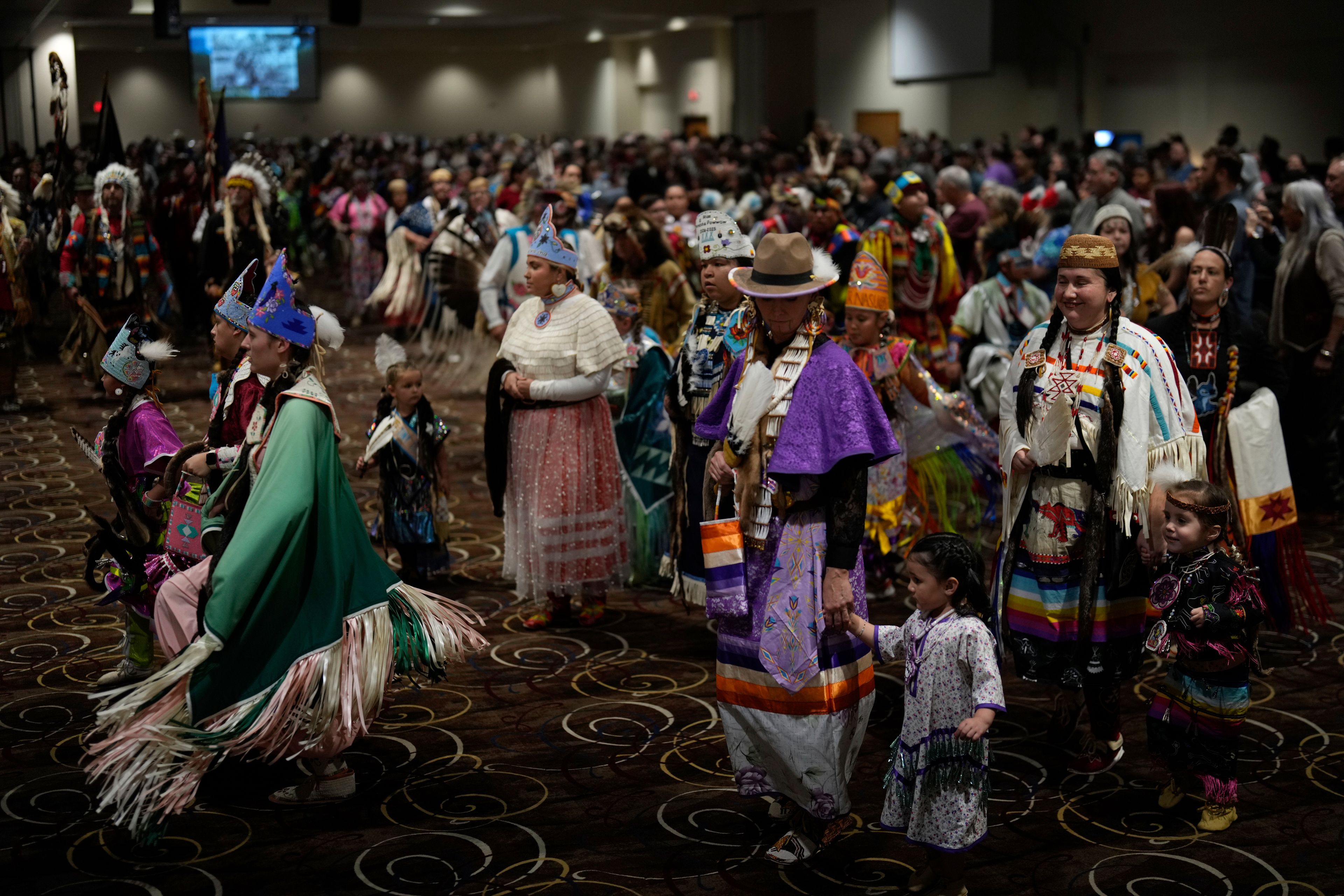 Tiffany Stuart, at right in white, holds hands with her daughter Kwestaani Chuski Stuart, bottom right, as they participate in a powwow at Chinook Winds Casino Resort, Saturday, Nov. 16, 2024, in Lincoln City, Ore. (AP Photo/Jenny Kane)