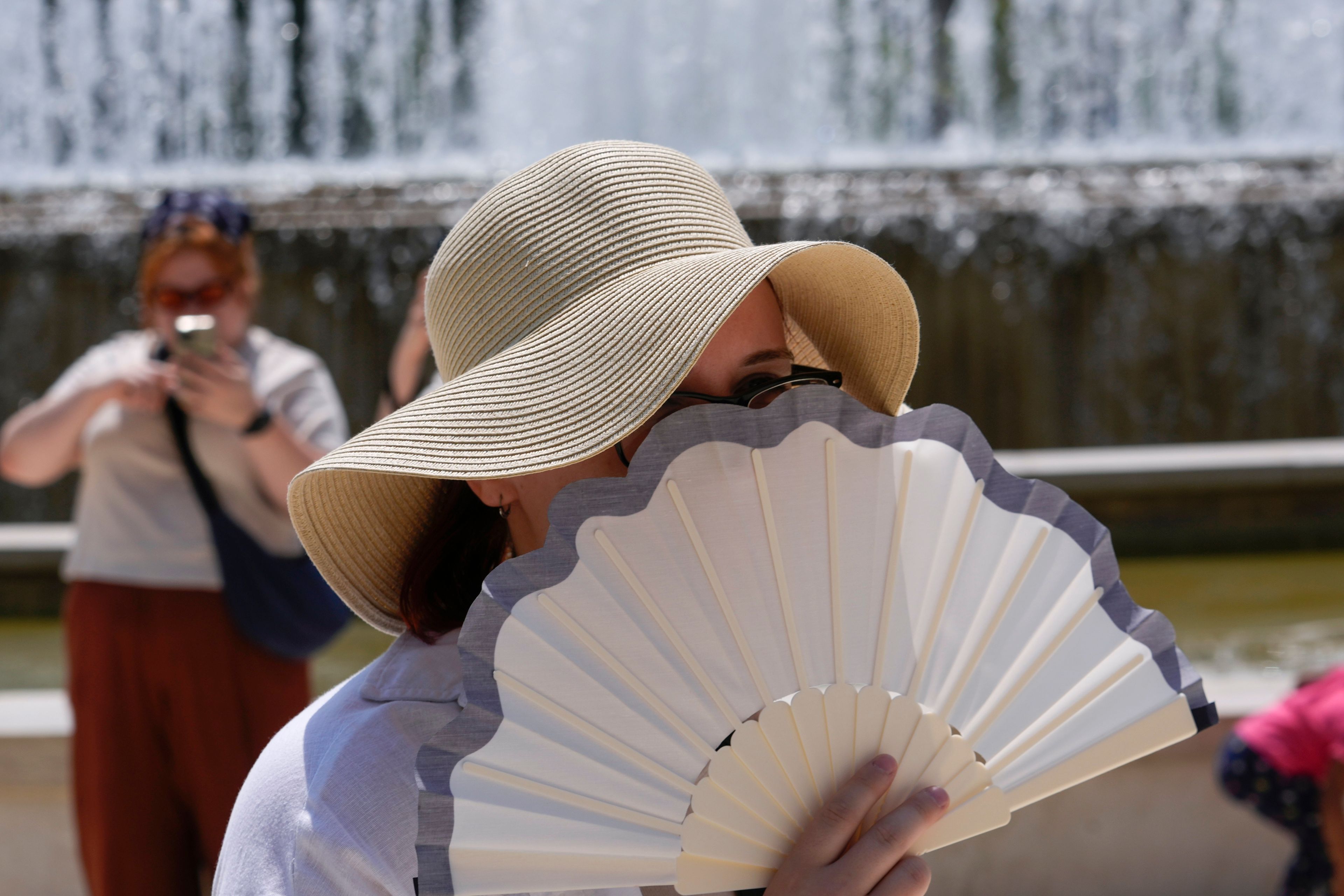 FILE - A tourist shelters from the sun by a fountain in front of the Sforzesco Castle in Milan, Italy, July 11, 2024. (AP Photo/Luca Bruno, File)