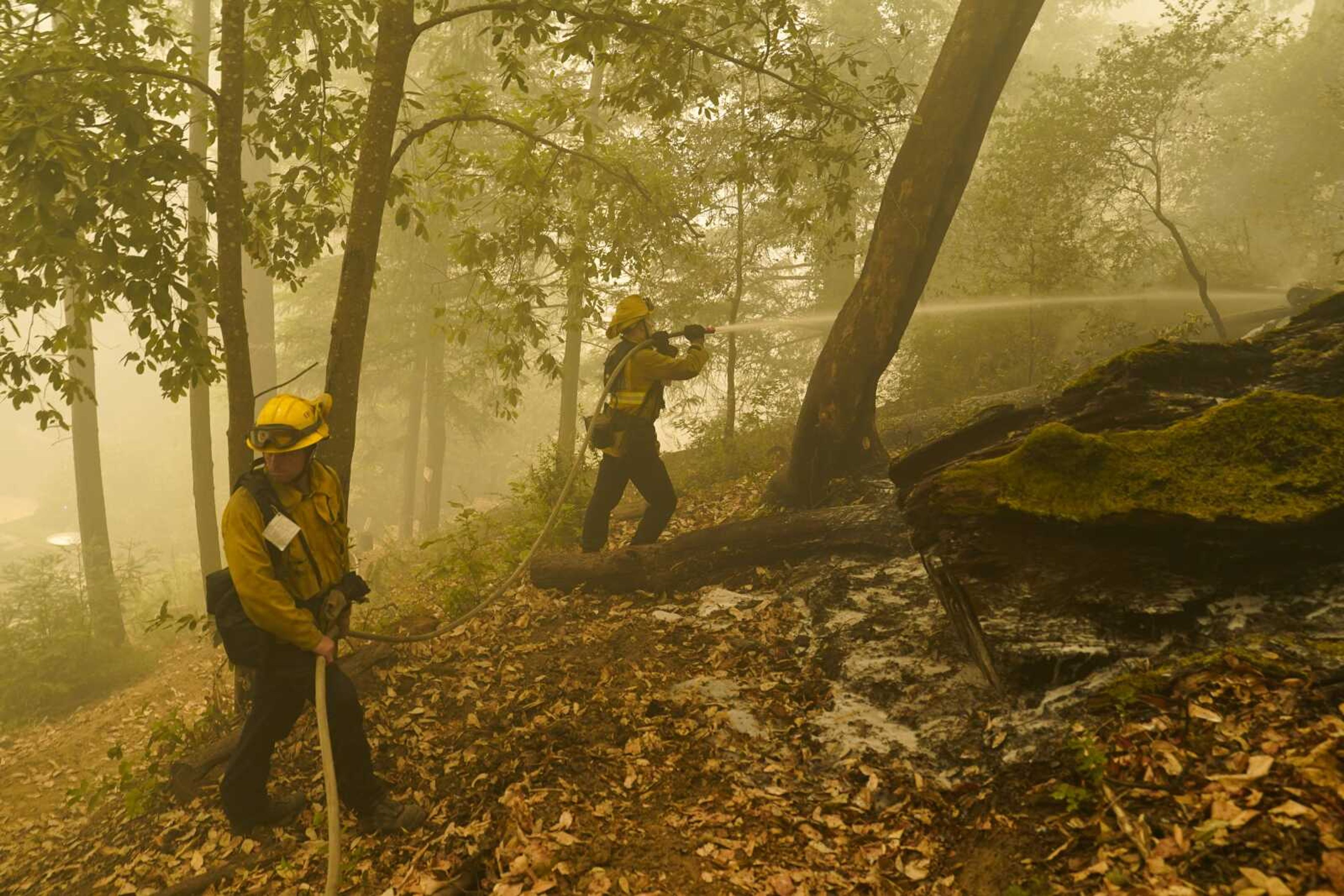 Firefighters, part of joint task force of South Pasadena and San Gabriel fire departments, hose down hot spots as smoke from the CZU August Lightning Complex Fire fills the air Saturday in Boulder Creek, California.