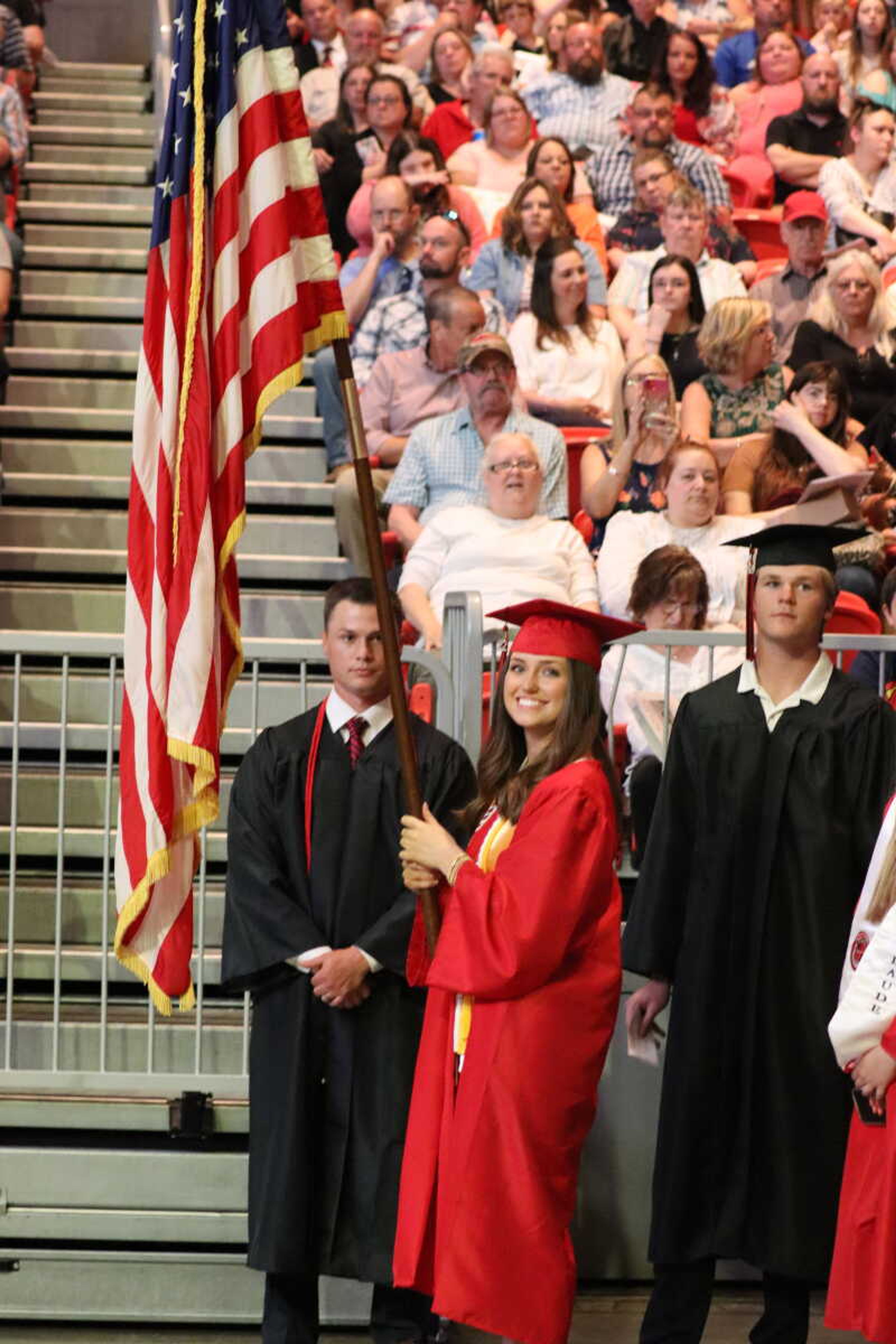 Student Body President Lydia Pobst smiling and carrying the American flag while leading in her graduating class.