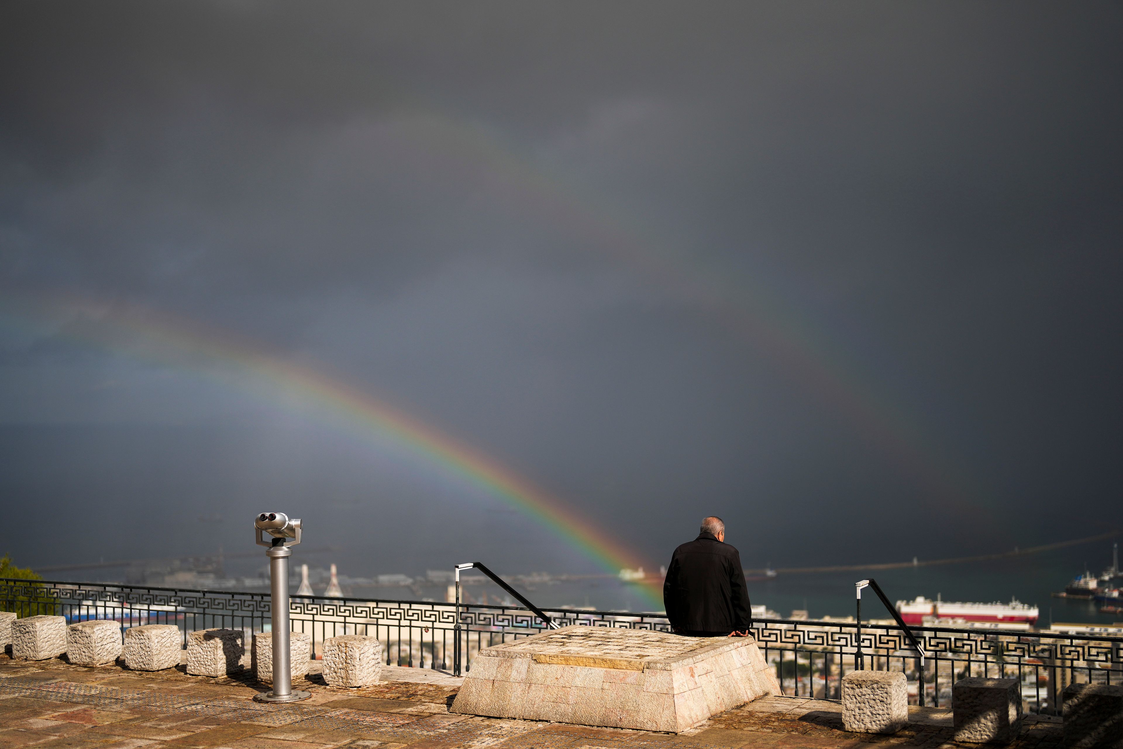 A double rainbow stretches across the sky as a man sits at a promenade overlooking Haifa, Israel, Tuesday, Nov. 26, 2024. (AP Photo/Francisco Seco)