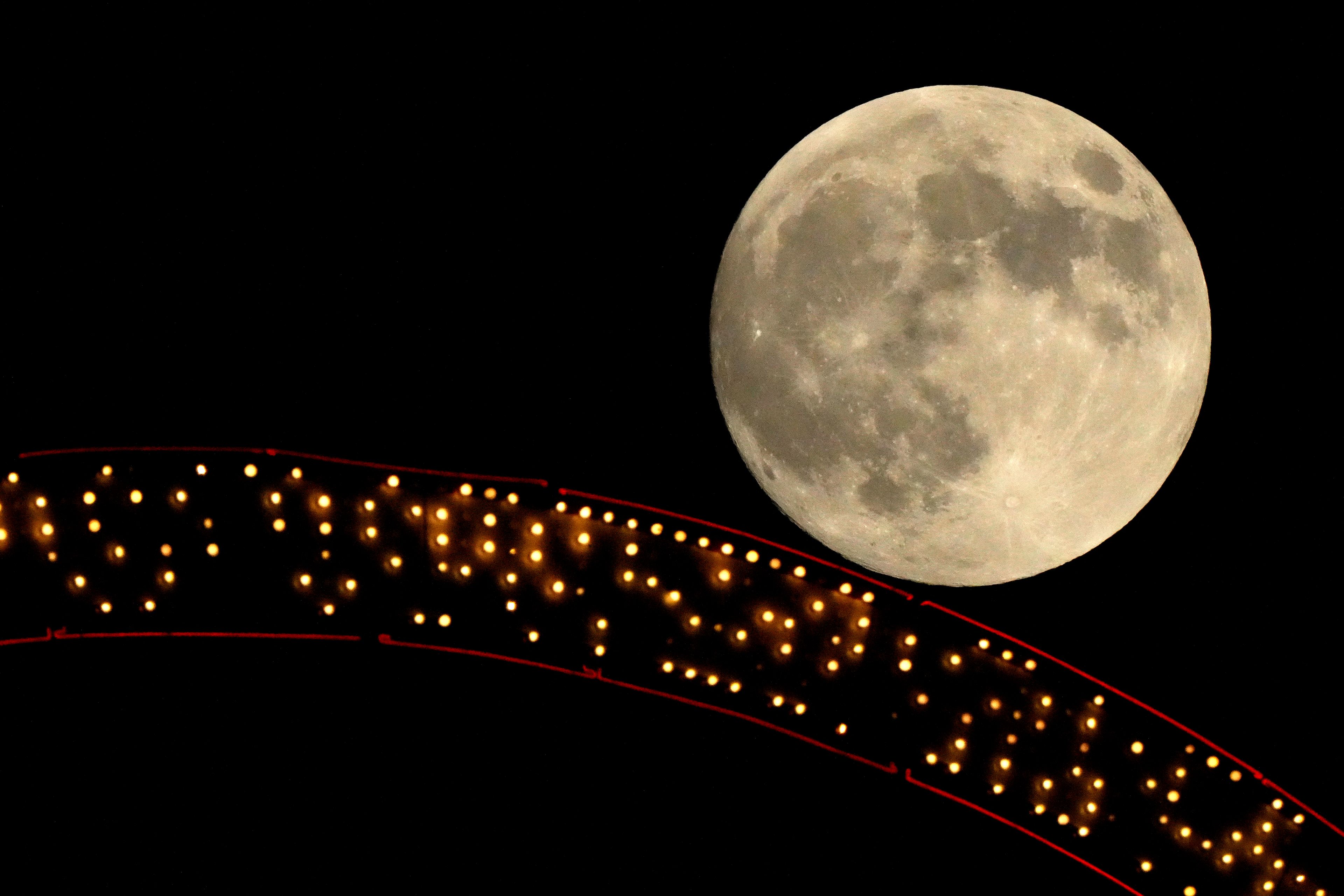 The moon rises beyond an antique sign atop a downtown apartment building, Wednesday, Oct. 16, 2024, in Kansas City, Mo. (AP Photo/Charlie Riedel)