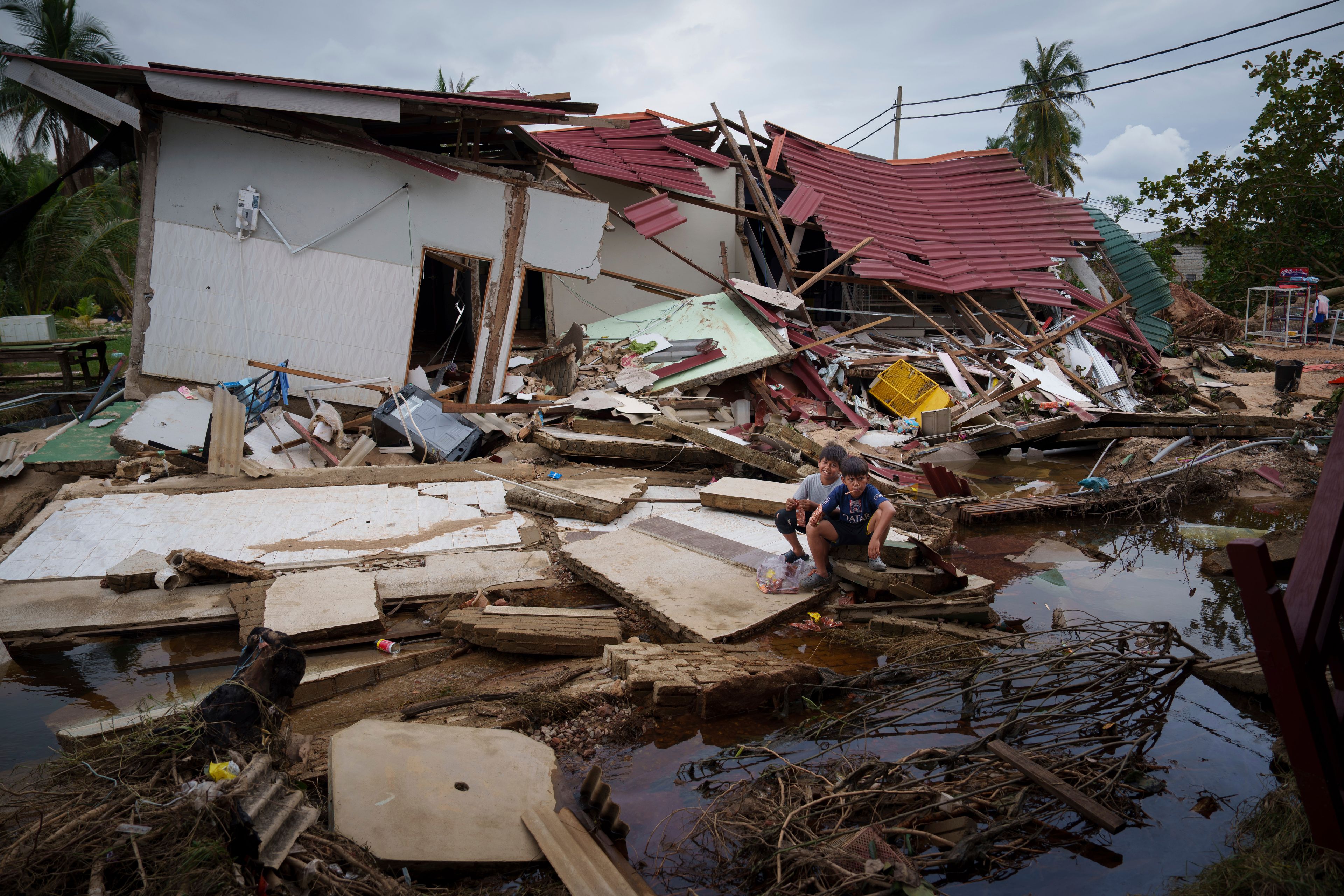 Children rest outside their house damaged by flood in Tumpat, on the outskirts of Kota Bahru, Malaysia, Tuesday, Dec. 3, 2024. (AP Photo/Vincent Thian)