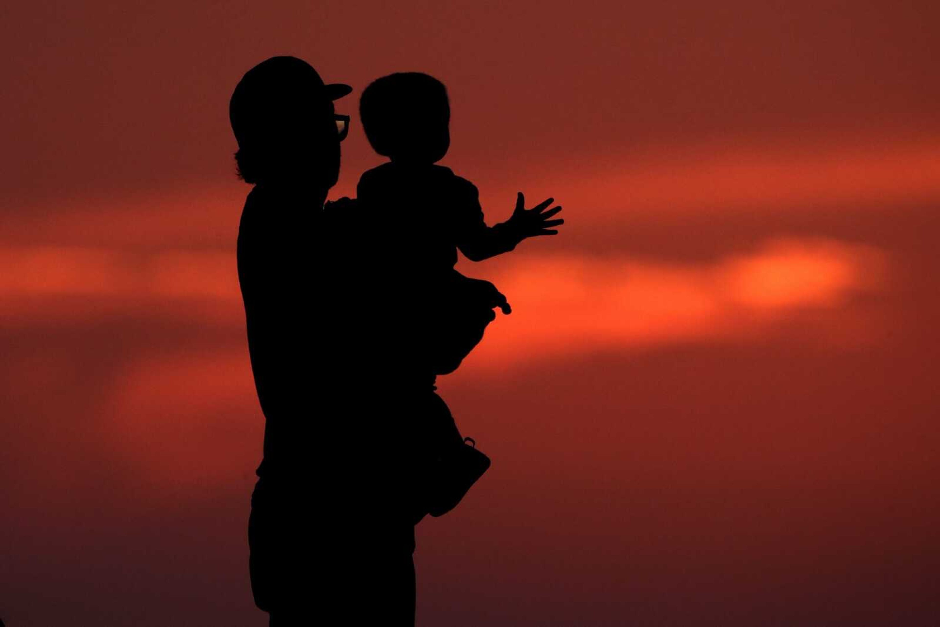 A man and his son are silhouetted against the sky as they watch the sunset from a park June 26 in Kansas City, Missouri.