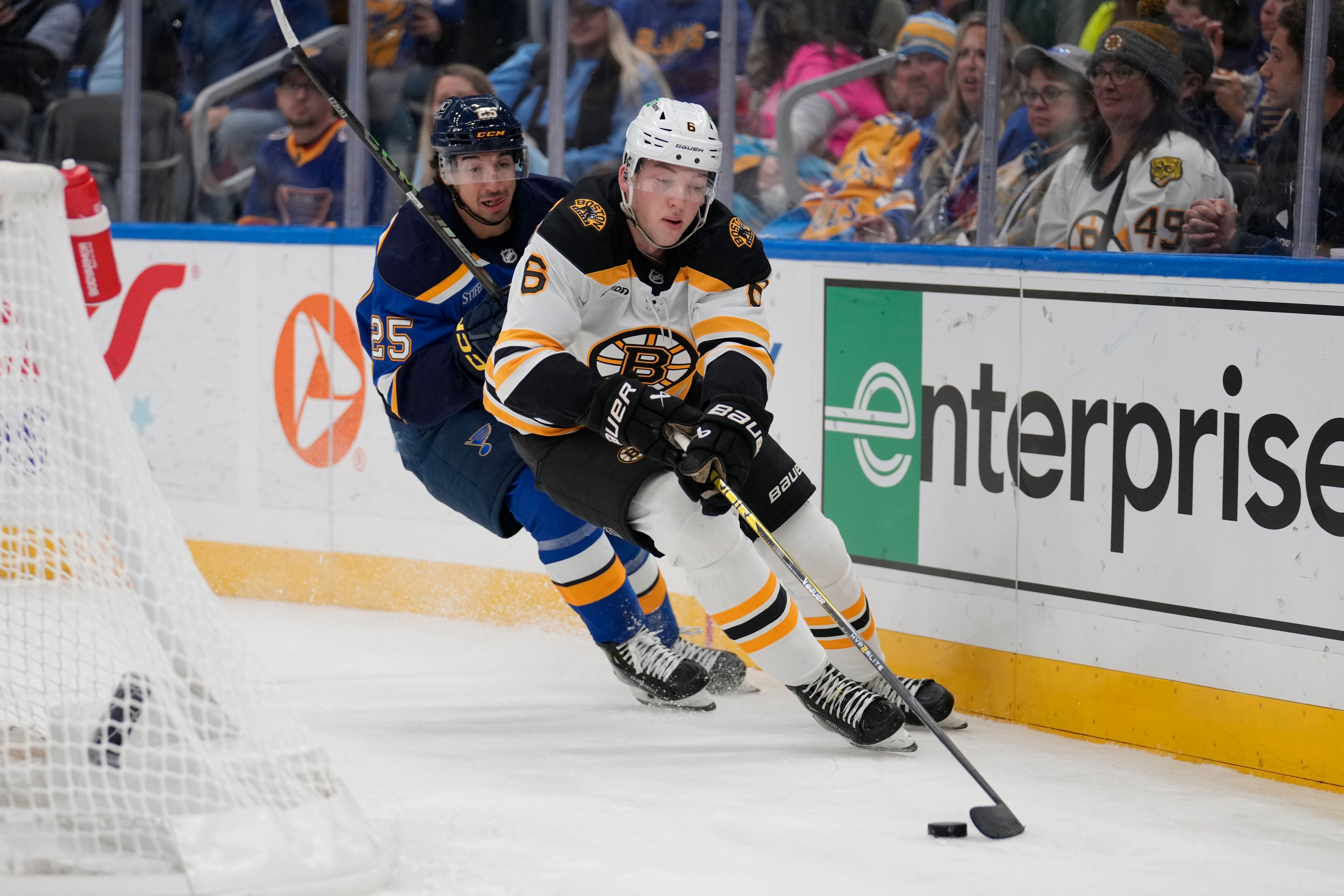 Boston Bruins' Mason Lohrei (6) chases after a loose puck along the boards as St. Louis Blues' Jordan Kyrou (25) watches during the second period of an NHL hockey game Tuesday, Nov. 12, 2024, in St. Louis. (AP Photo/Jeff Roberson)